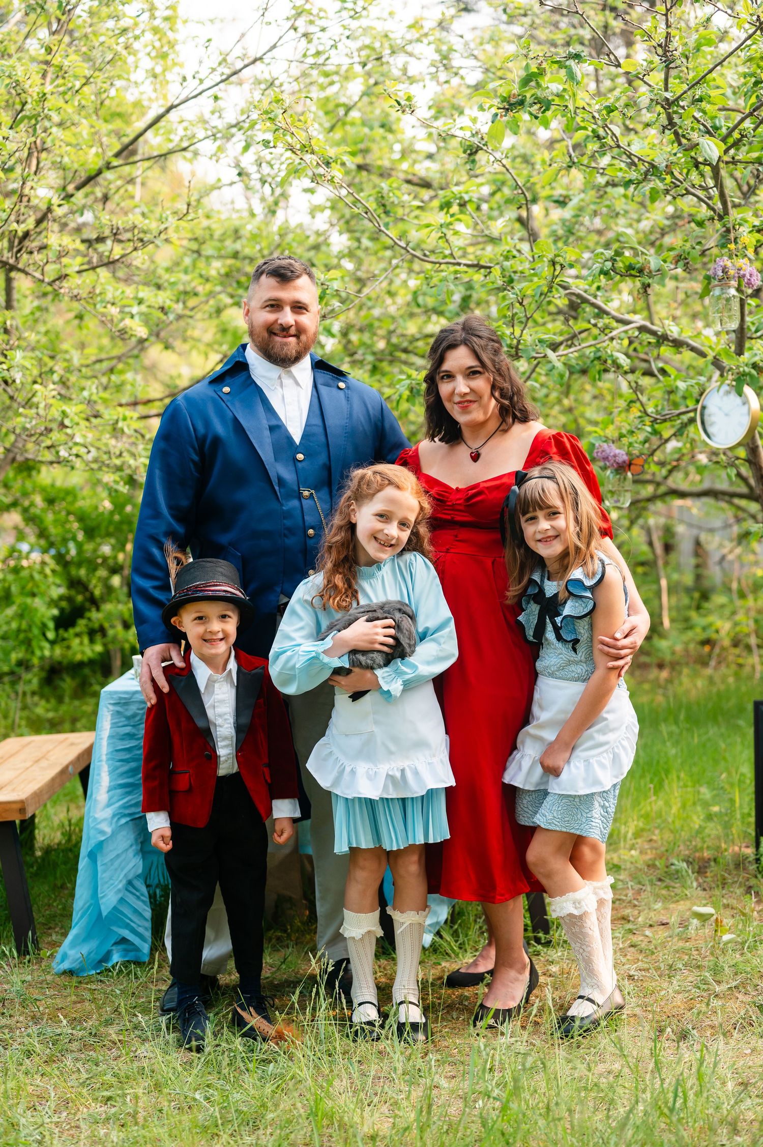 Family dressed in Alice in Wonderland-inspired outfits poses together in a spring garden setting.