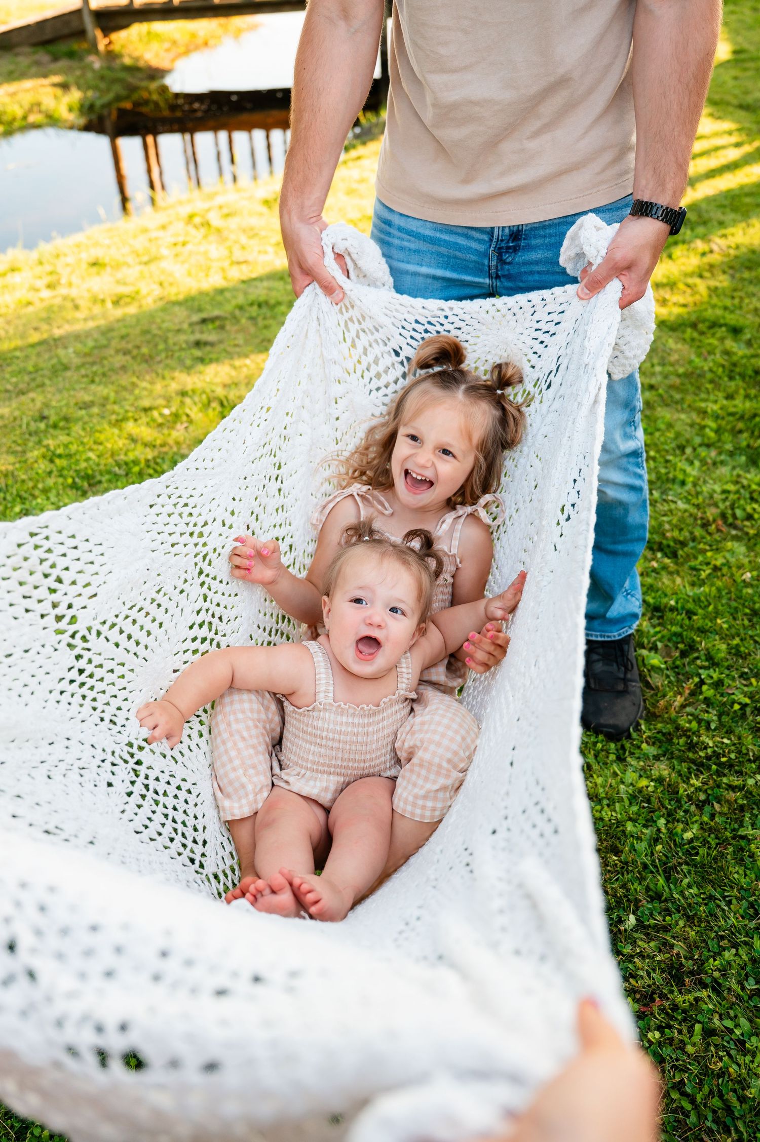 Two children laughing while playing in a white macrame hammock on a summers  day.