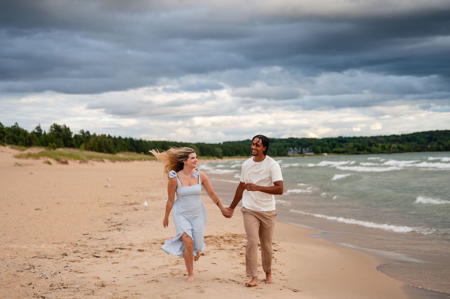 Couple running along beach with stormy clouds overhead.