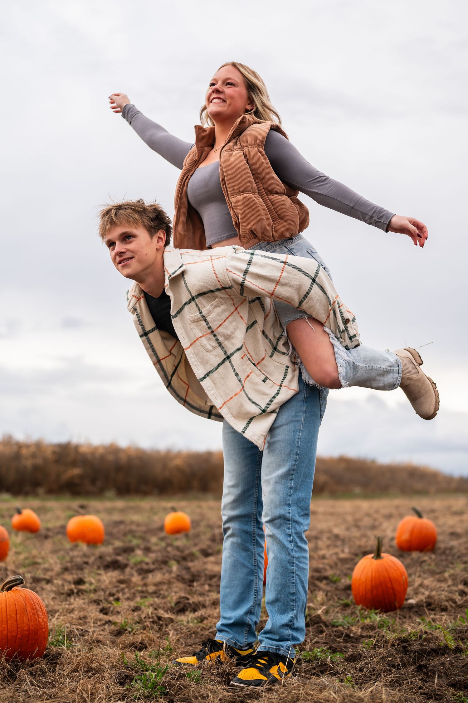 A playful moment captured in a pumpkin patch with fall colors and cloudy skies.