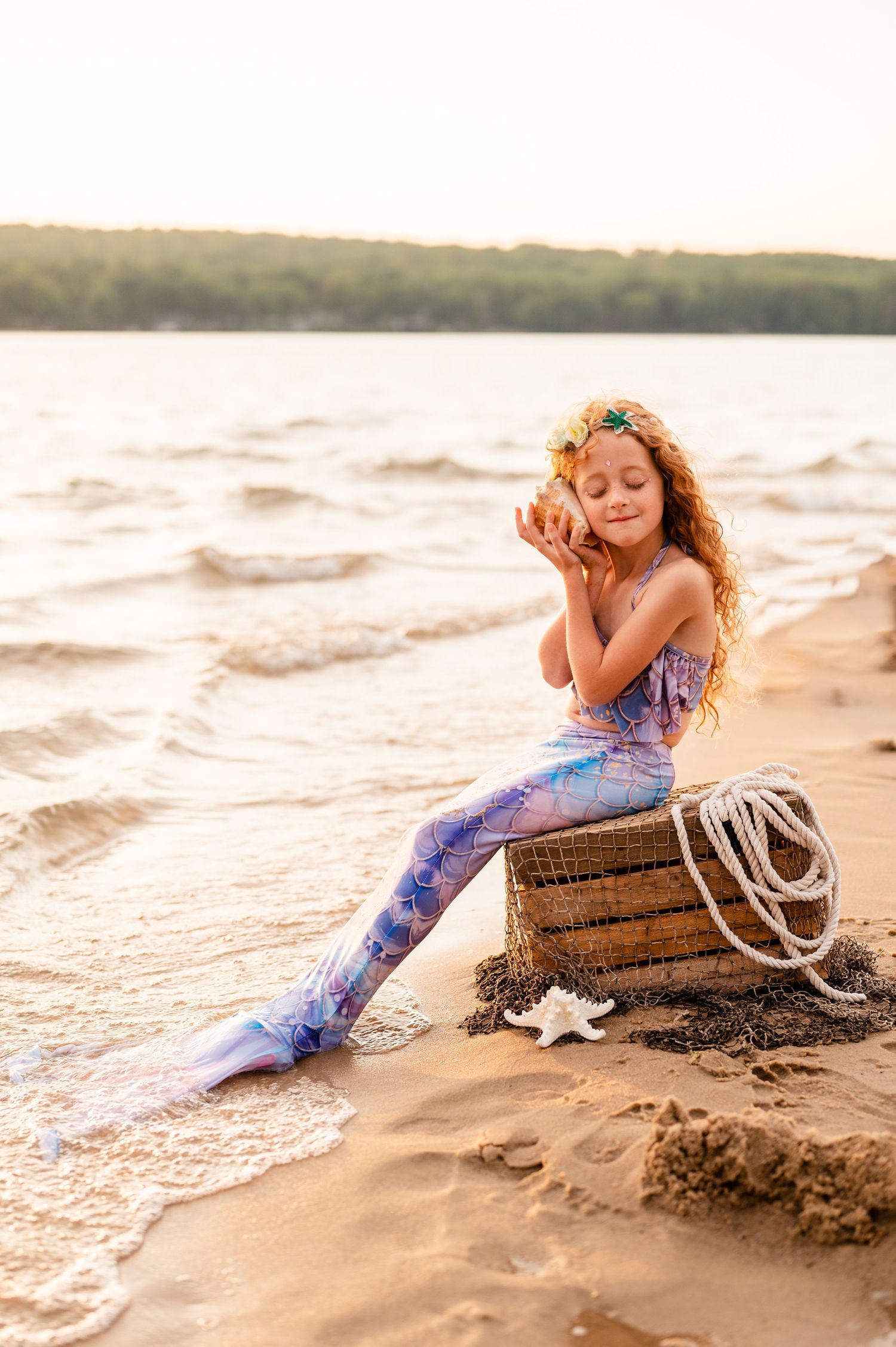 Whimsical beach photography with mermaid costume and wooden prop at sunset.