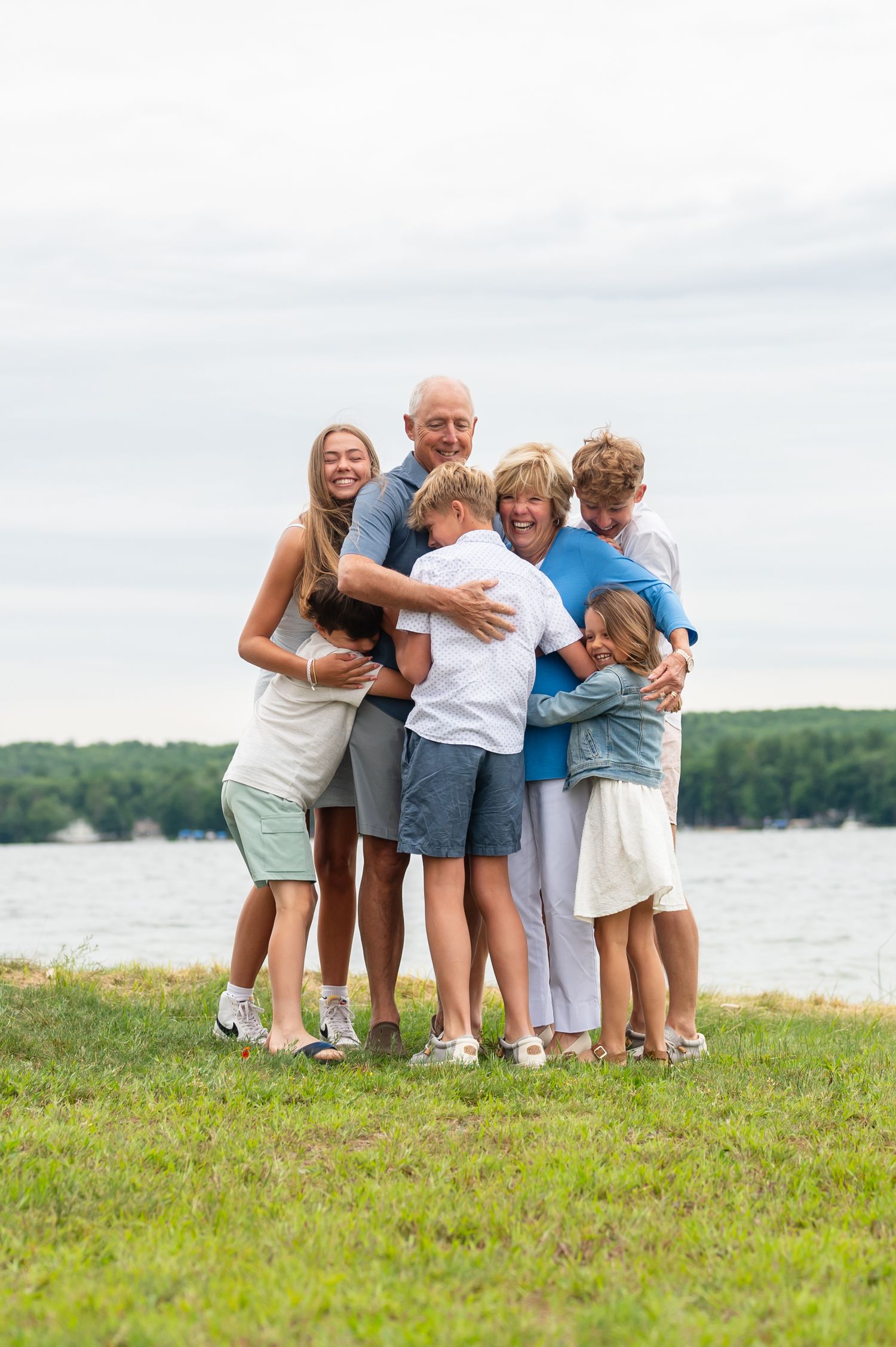 Family members huddled together in playful pose on the grass by a lake.