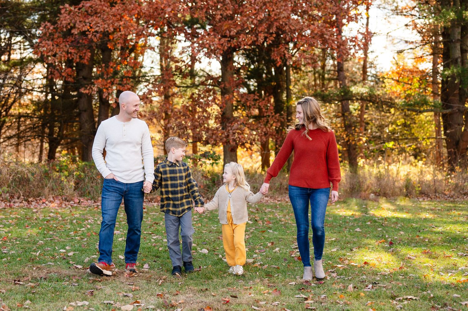 Family walking together through autumn trees at sunset with warm golden light filtering through leaves.