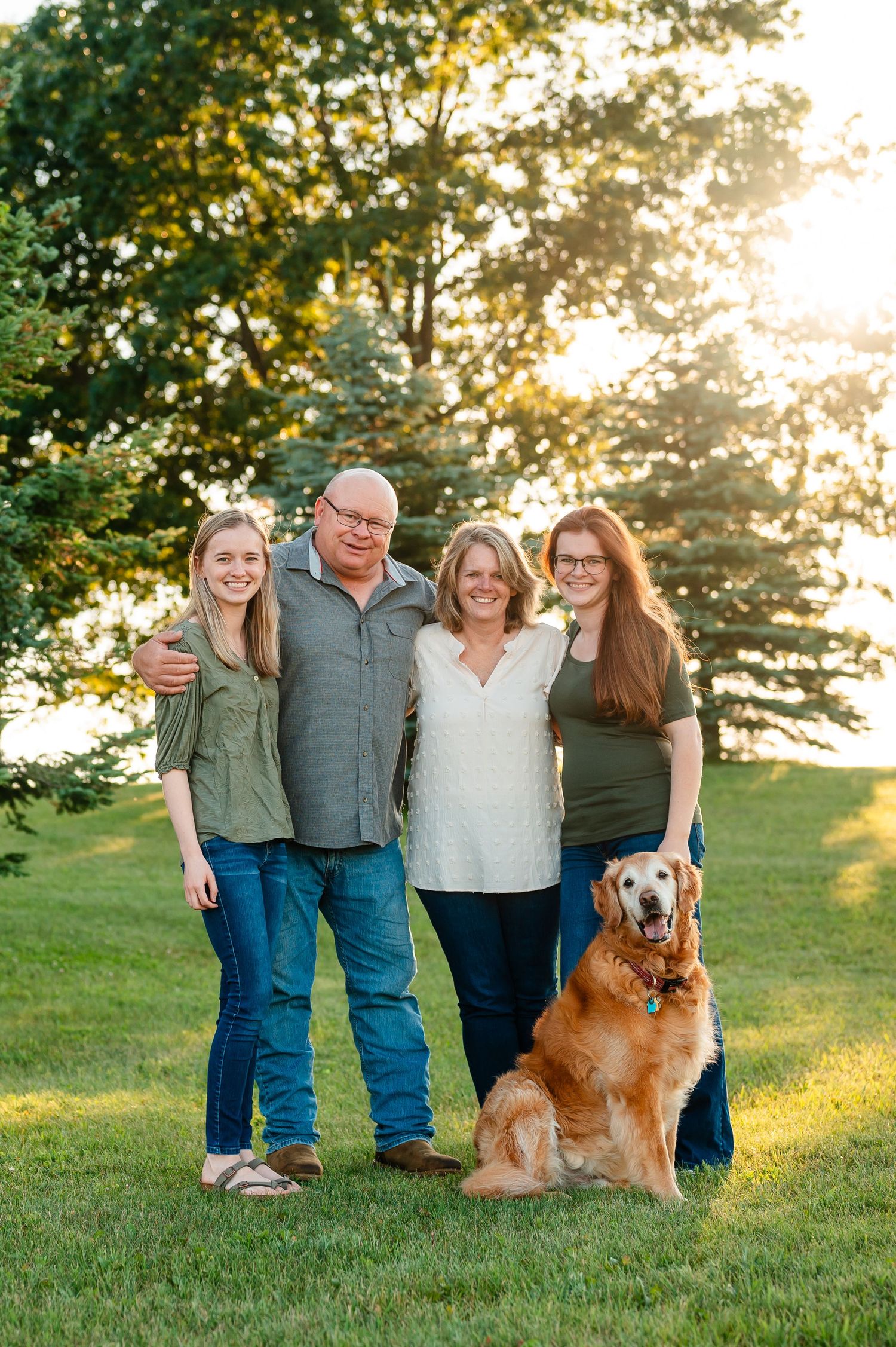 Family portrait on grassy hill with golden retriever dog at sunset.