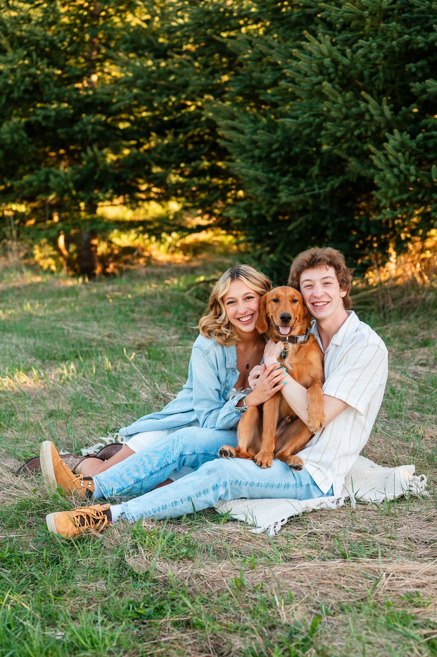 Couple relaxing on grassy hill with their golden retriever during golden hour.