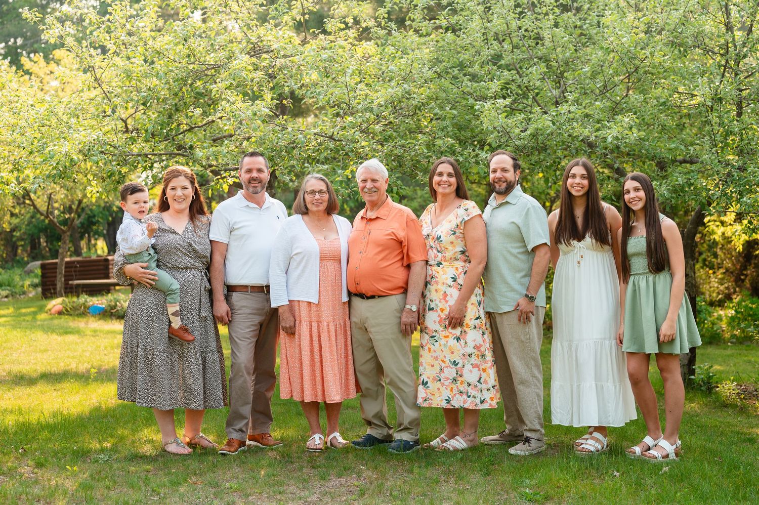 An extended family session coordinated in pastel outfits pose together for a family photo in a sunny garden setting.