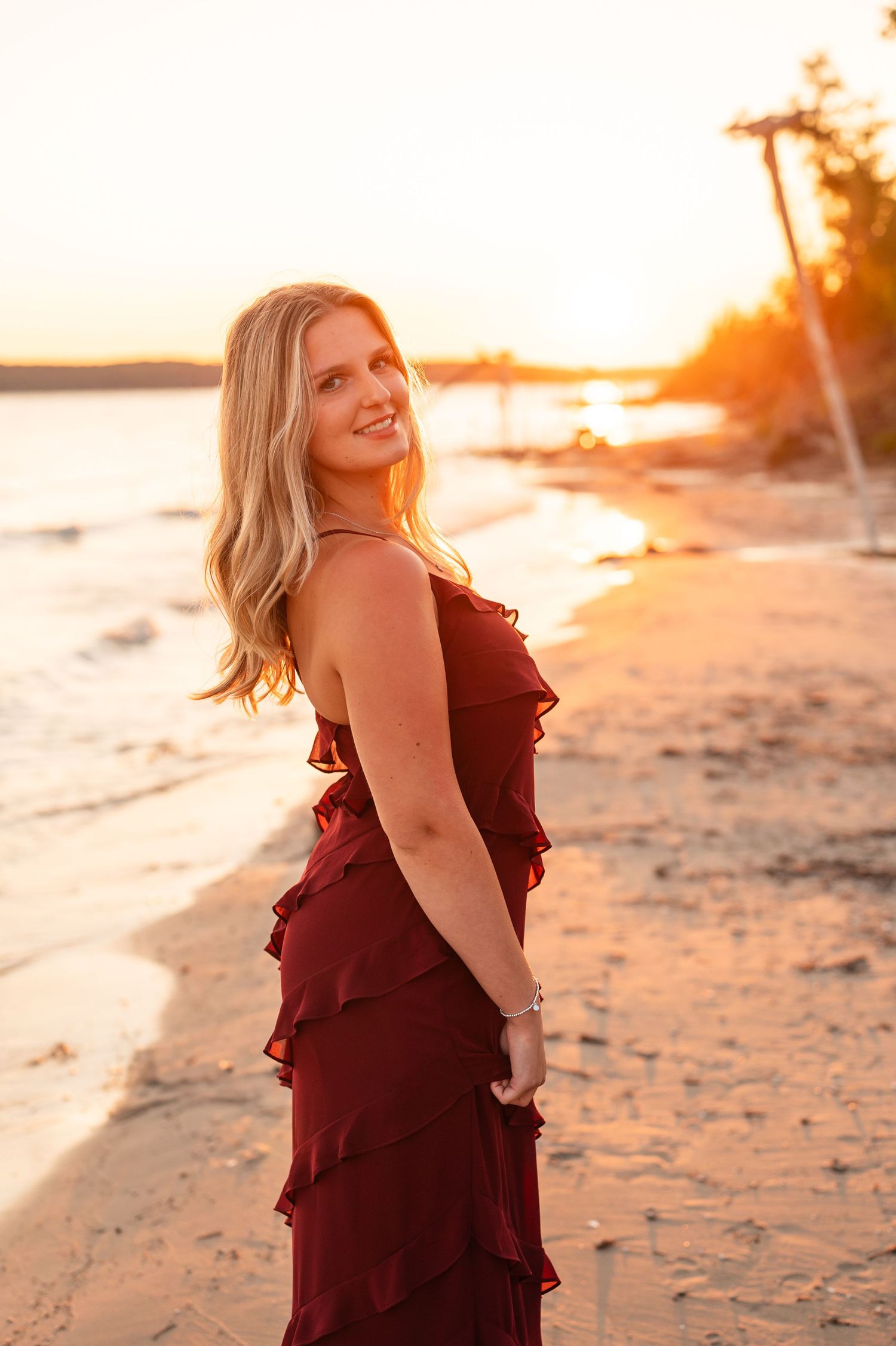 A burgundy dress glows warmly in the golden sunset light on a sandy beach.