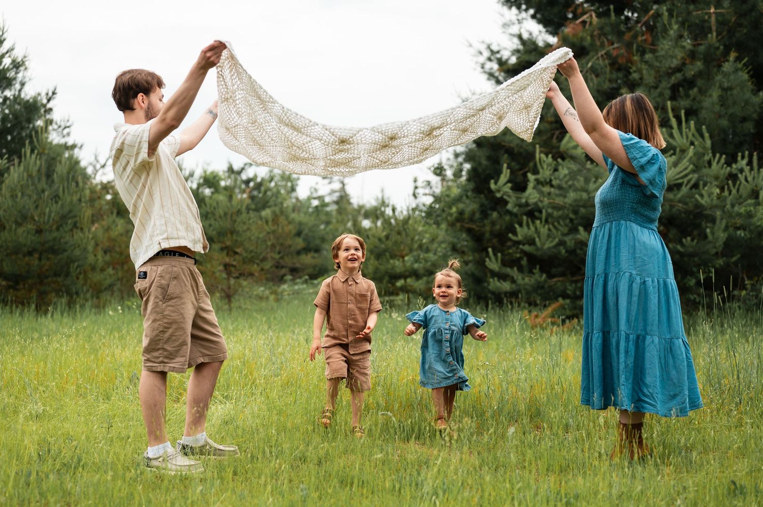 Family plays with a white lace blanket in a grassy field creating joyful moments.