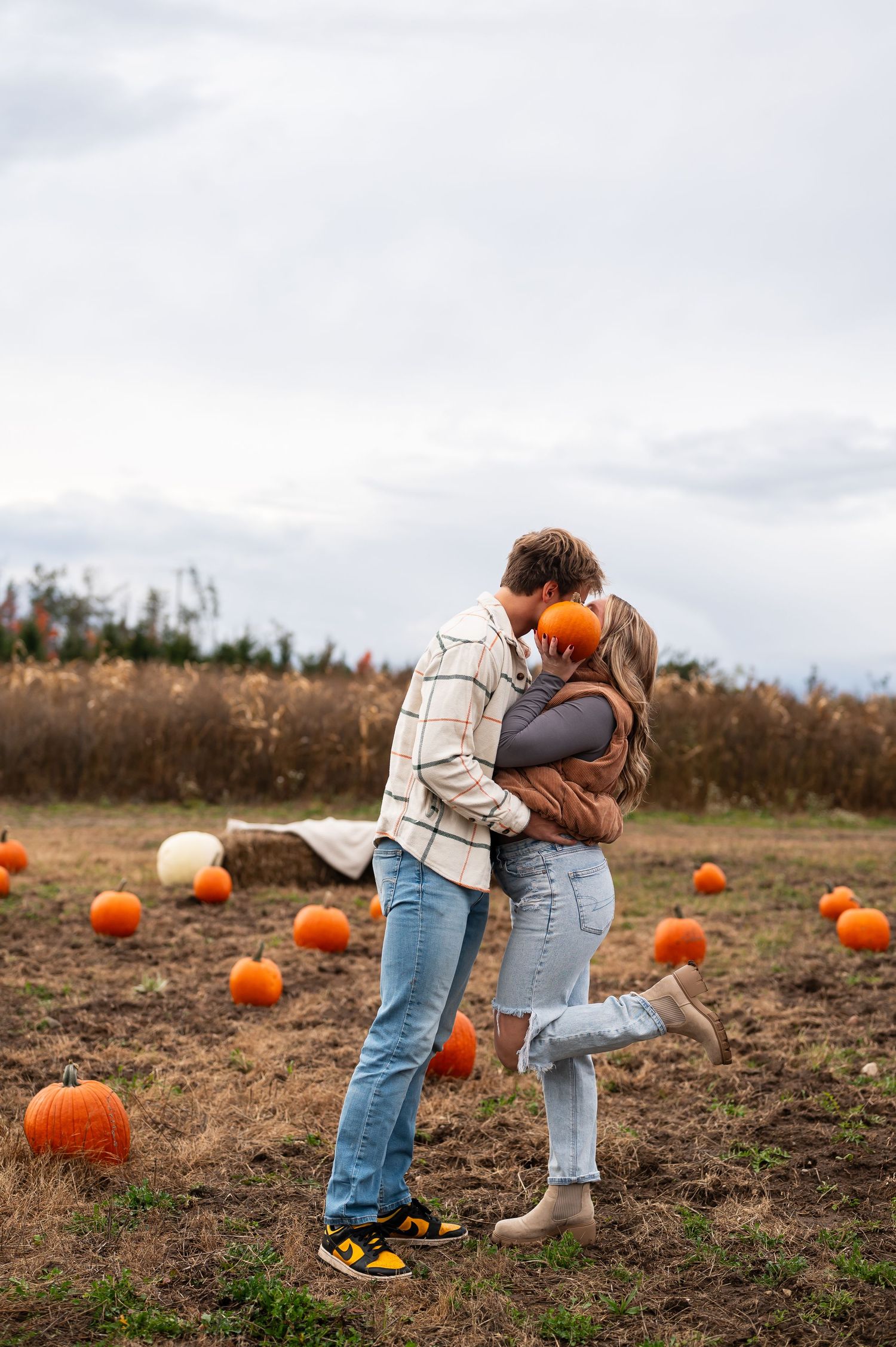 Romantic couple embraces in a pumpkin patch during autumn season.