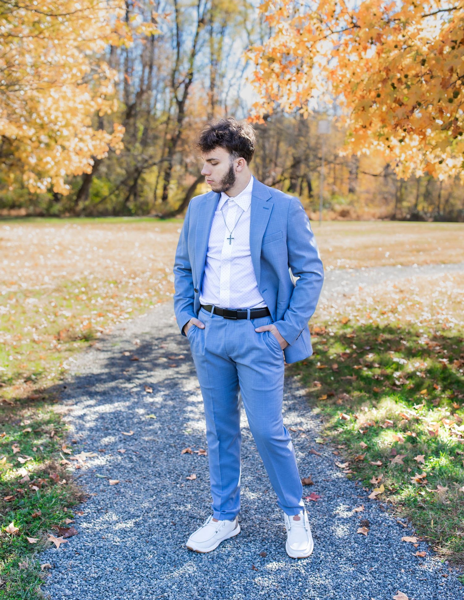 Person in powder blue suit walks along gravel path surrounded by fall leaves.