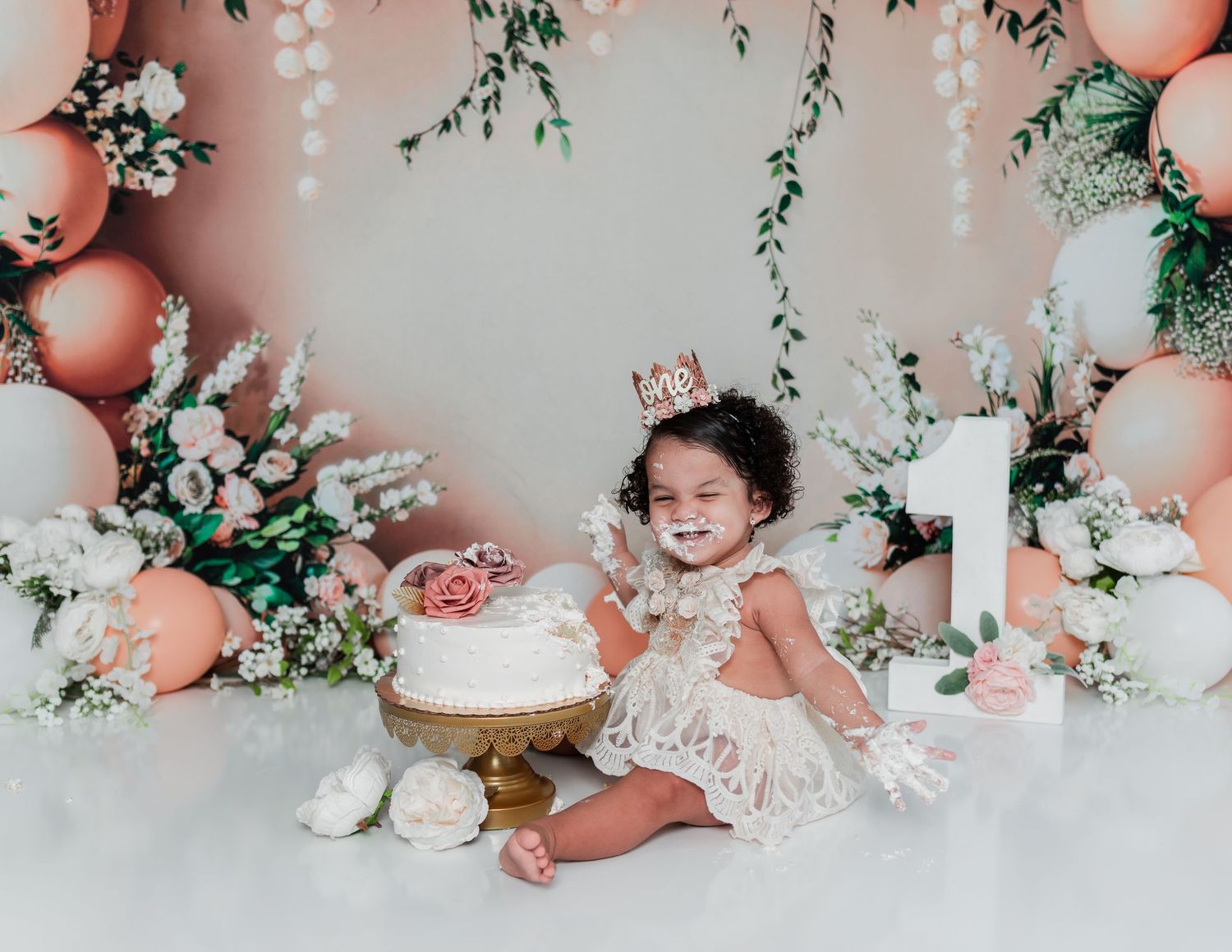 First birthday setup with peach and white decor featuring floral arrangements and balloons.