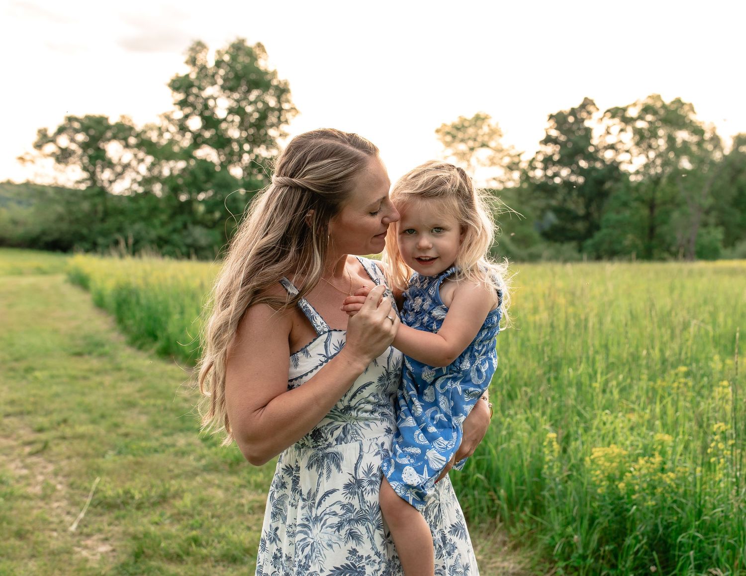 Sweet candid moment shared between family members in a sunlit meadow setting.