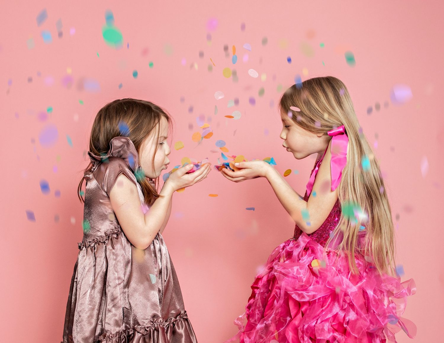 Kids playing with falling confetti in festive pink photo session setup.