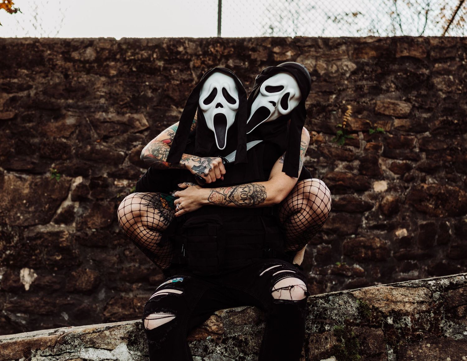Gothic themed photoshoot with black clothing against stone wall and autumn leaves.