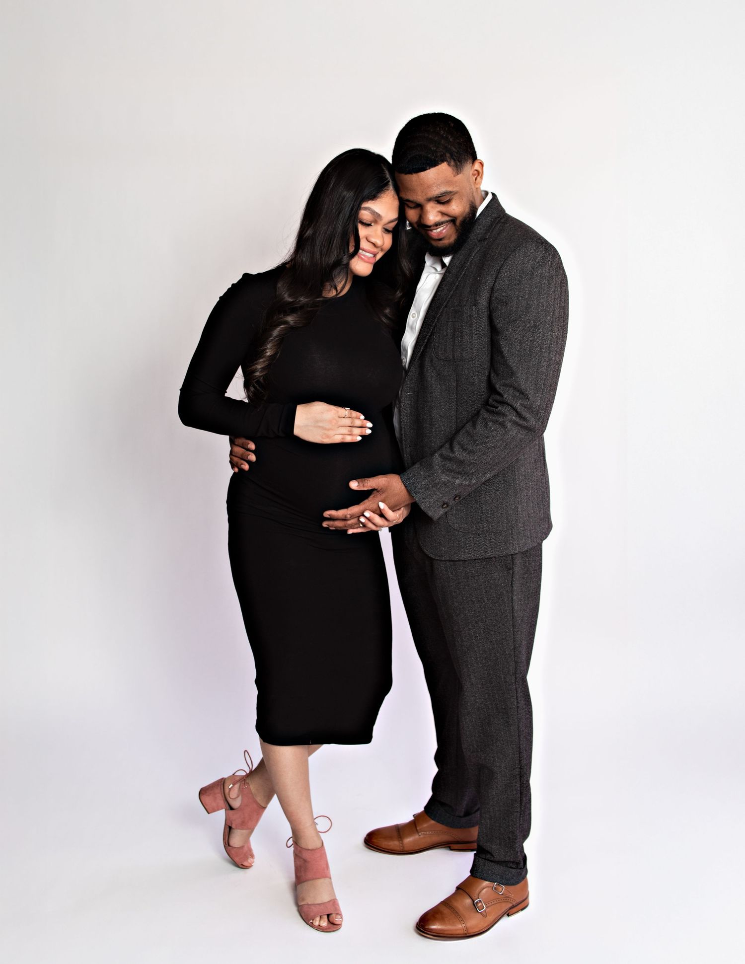 Maternity photoshoot with couple in black outfits against white backdrop.