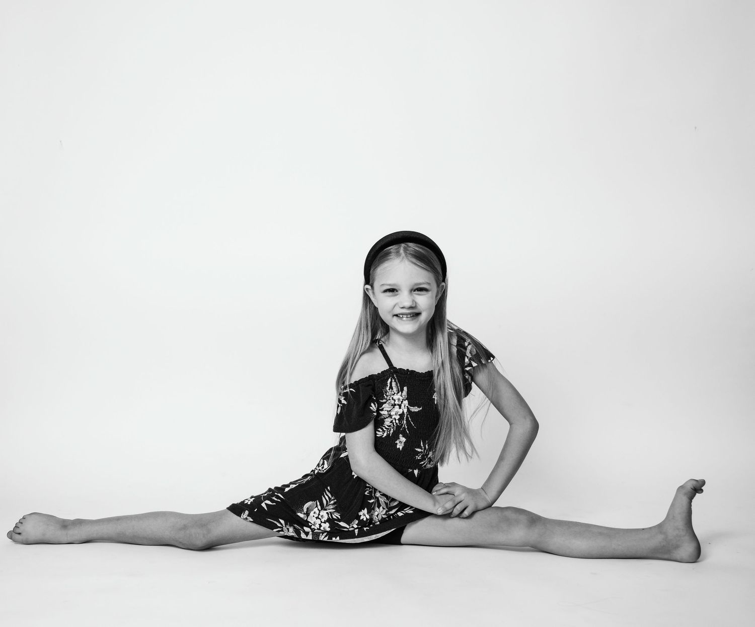 A black and white portrait showing a full split pose in a floral dress.