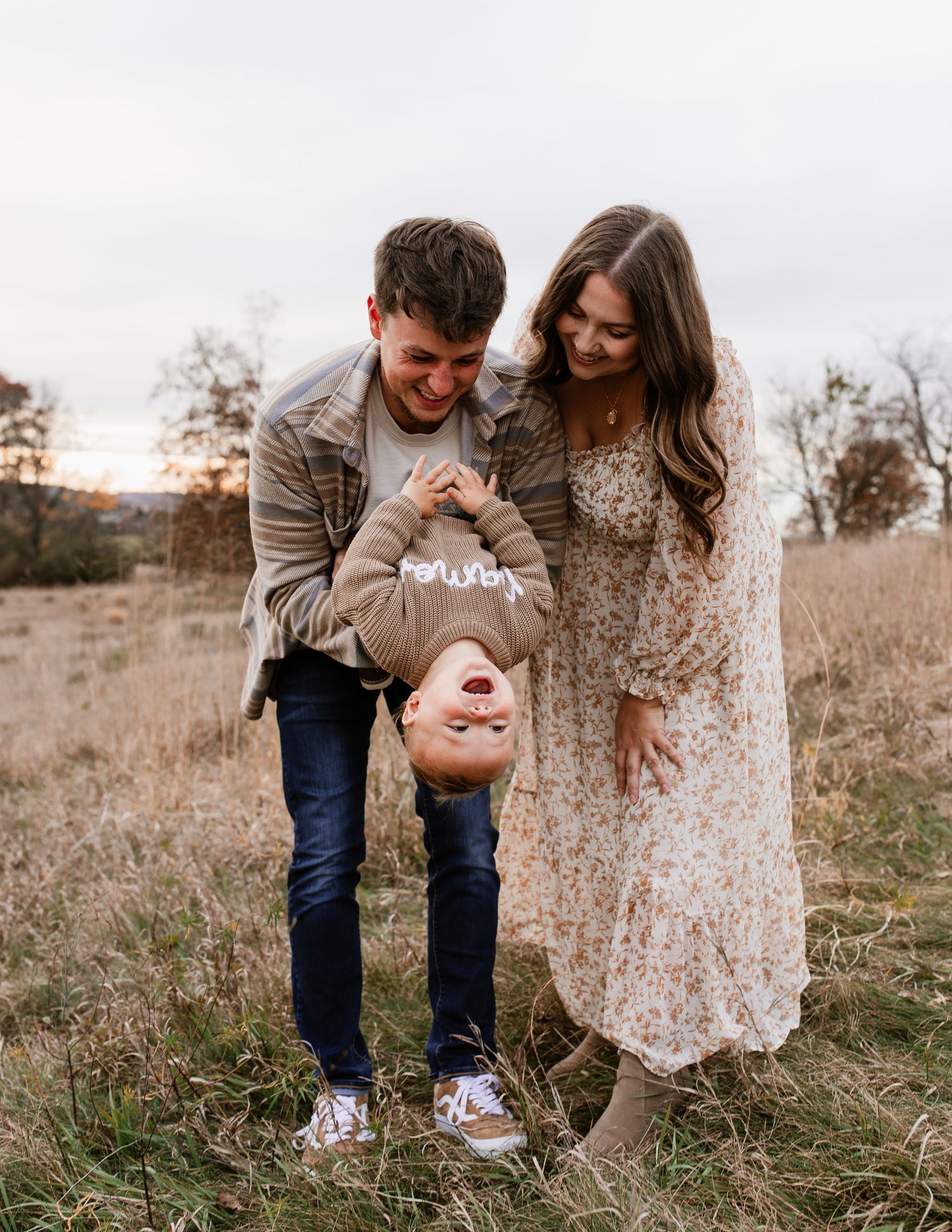 Playful couple sharing laughter while dancing in a rustic field setting.