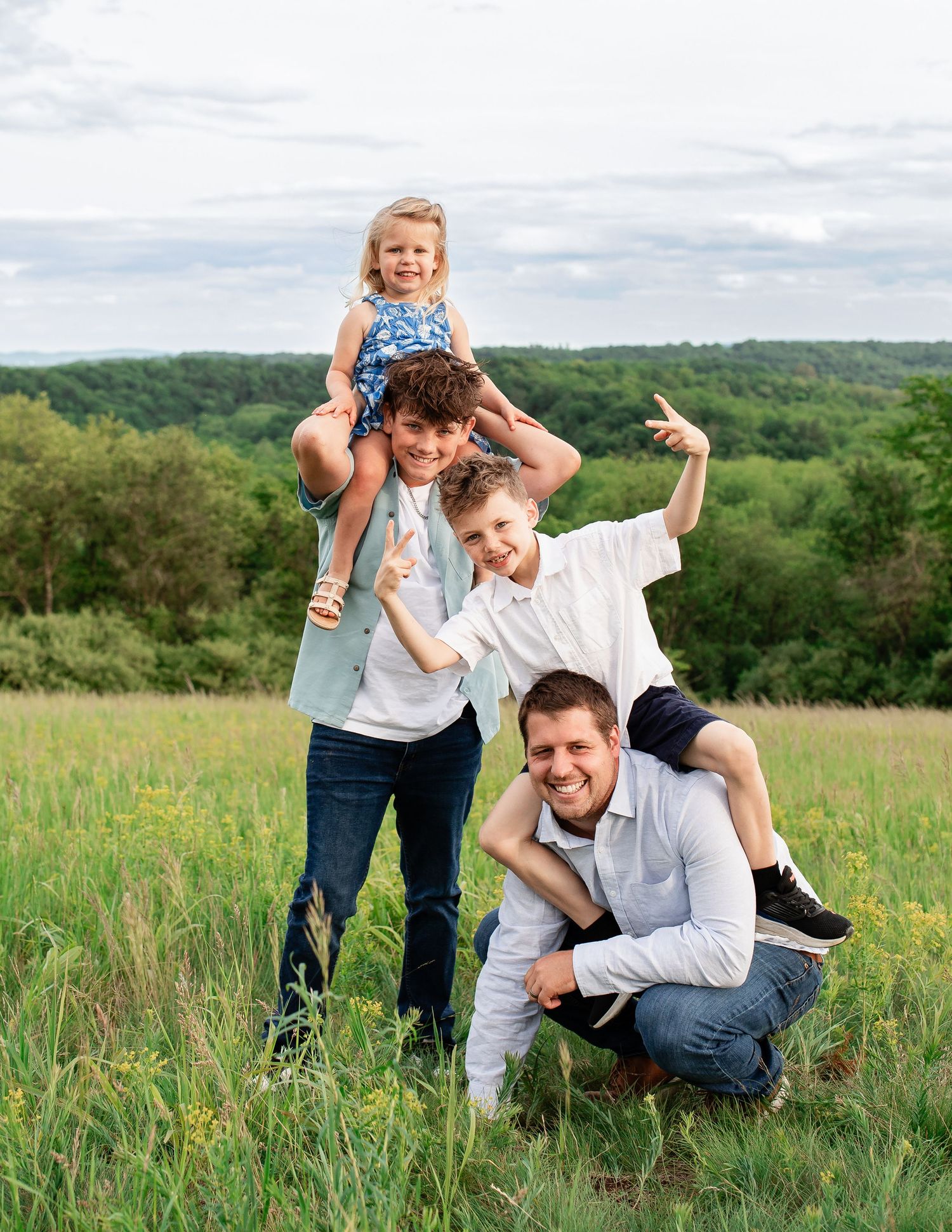 Family enjoying playful moments together in a scenic meadow with rolling green hills in the background.