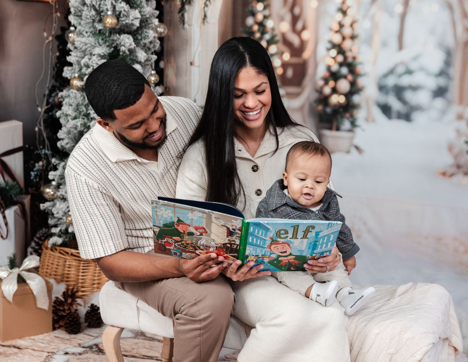 Family reading a book together on white blanket with decorated winter scene backdrop.