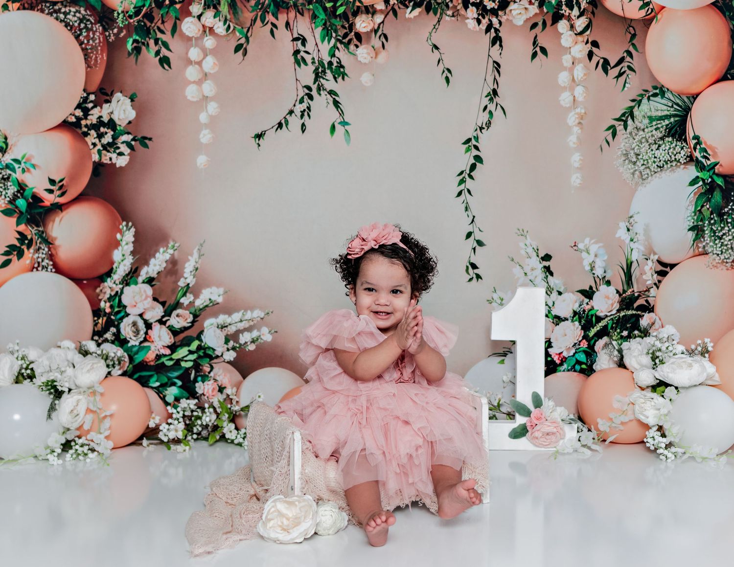 Smiling baby celebrating milestone with pink decor, balloons, and floral arrangements.