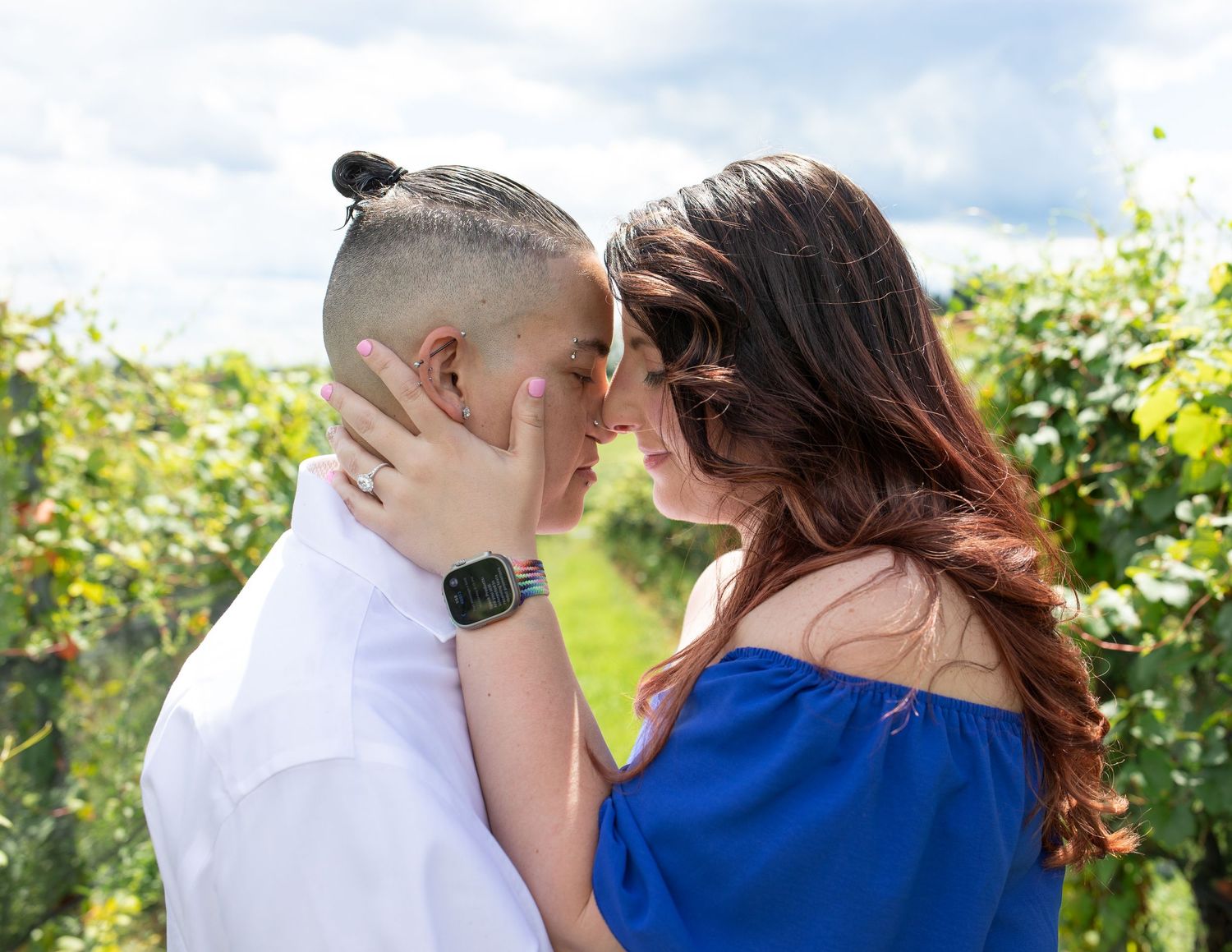 Couple embracing in a sunlit vineyard with green vines surrounding them.