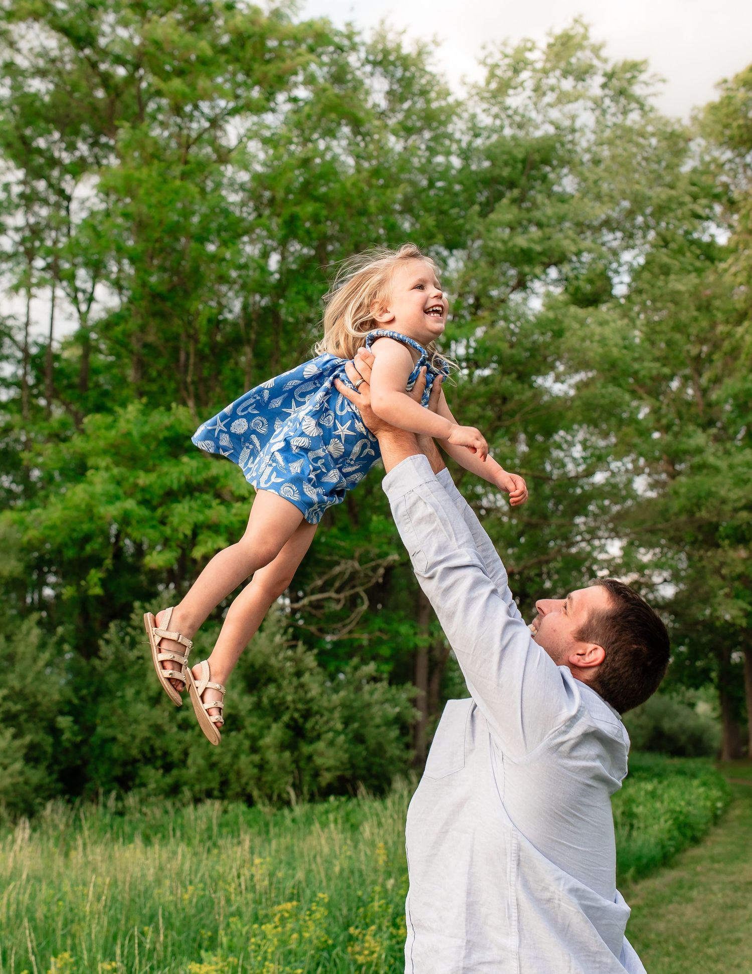 Joyful outdoor playtime scene with child being lifted high in the air against a green summer background.