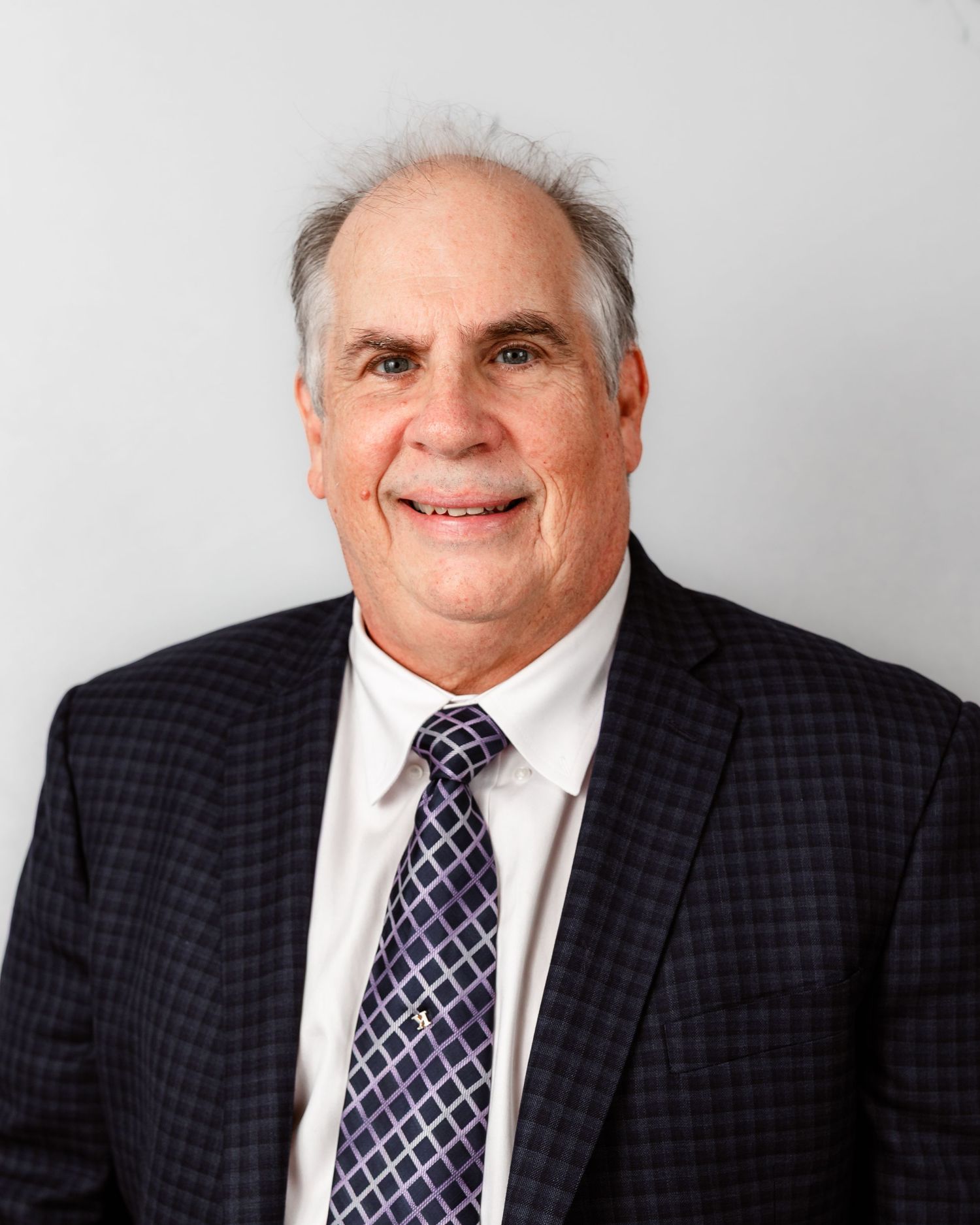 Professional headshot of executive in checkered suit and striped tie.
