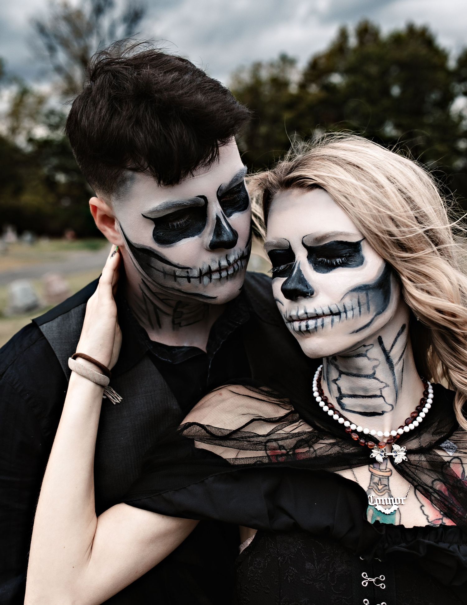 Couple wearing skull face paint poses together in dramatic black and white style.
