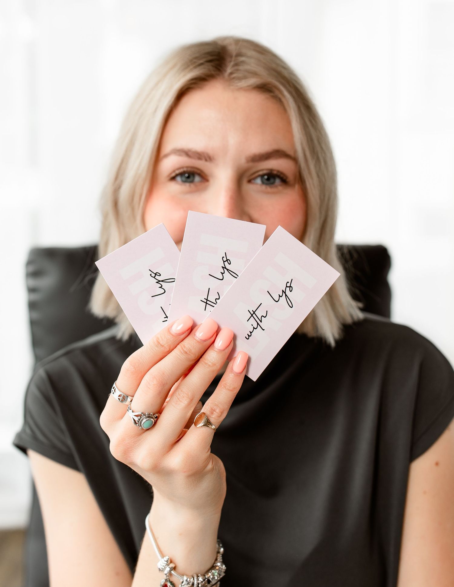 Person in black shirt holds up playing cards while sitting on dark couch.