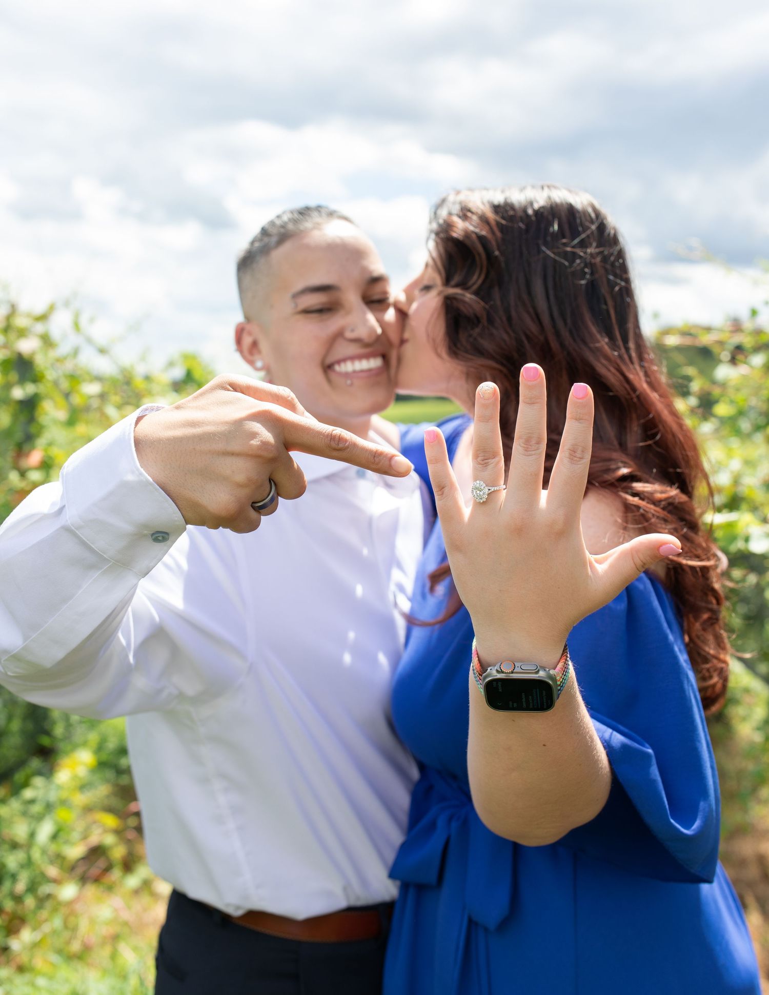 Newly engaged couple showing off ring in vineyard setting.