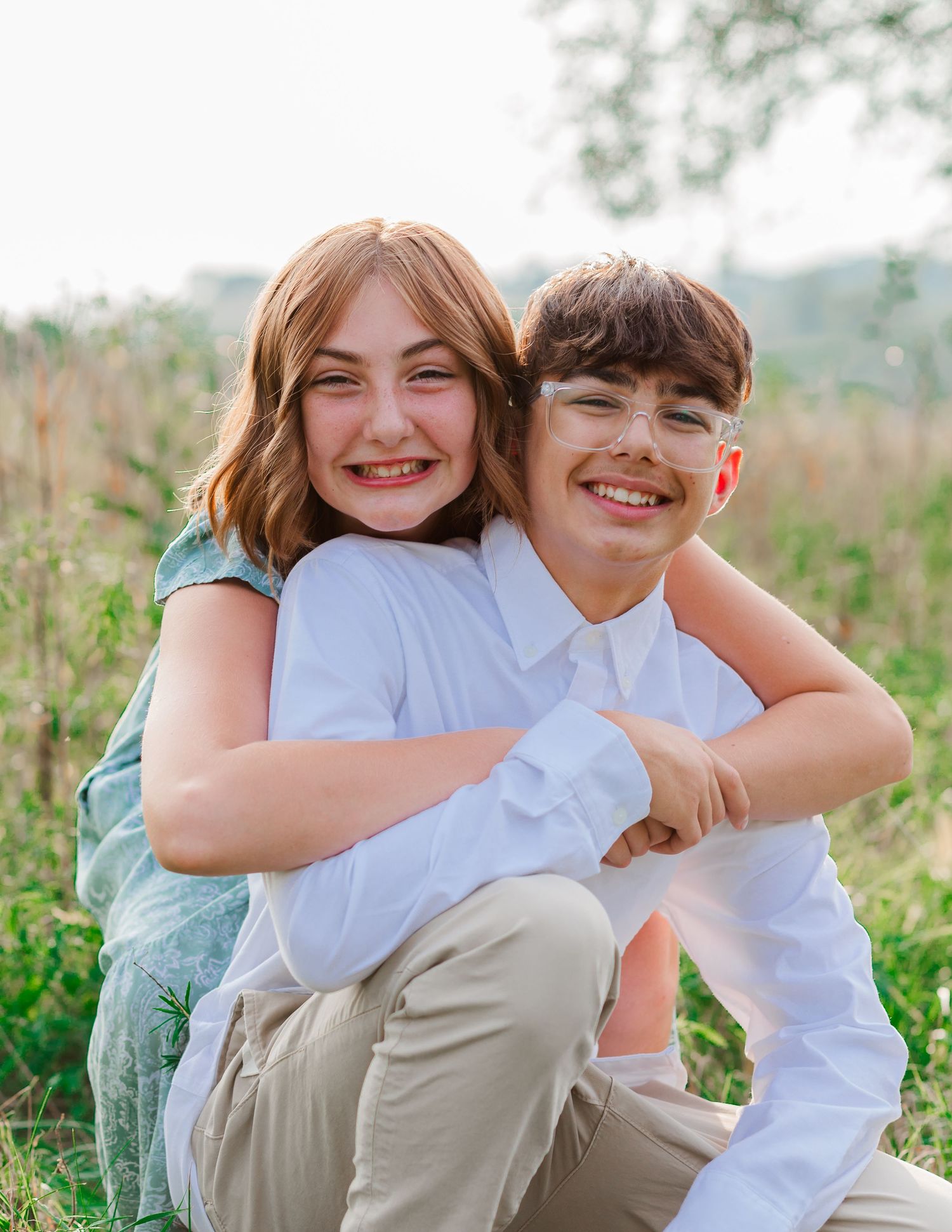 Siblings sharing laughs while sitting together in a sunny outdoor setting.