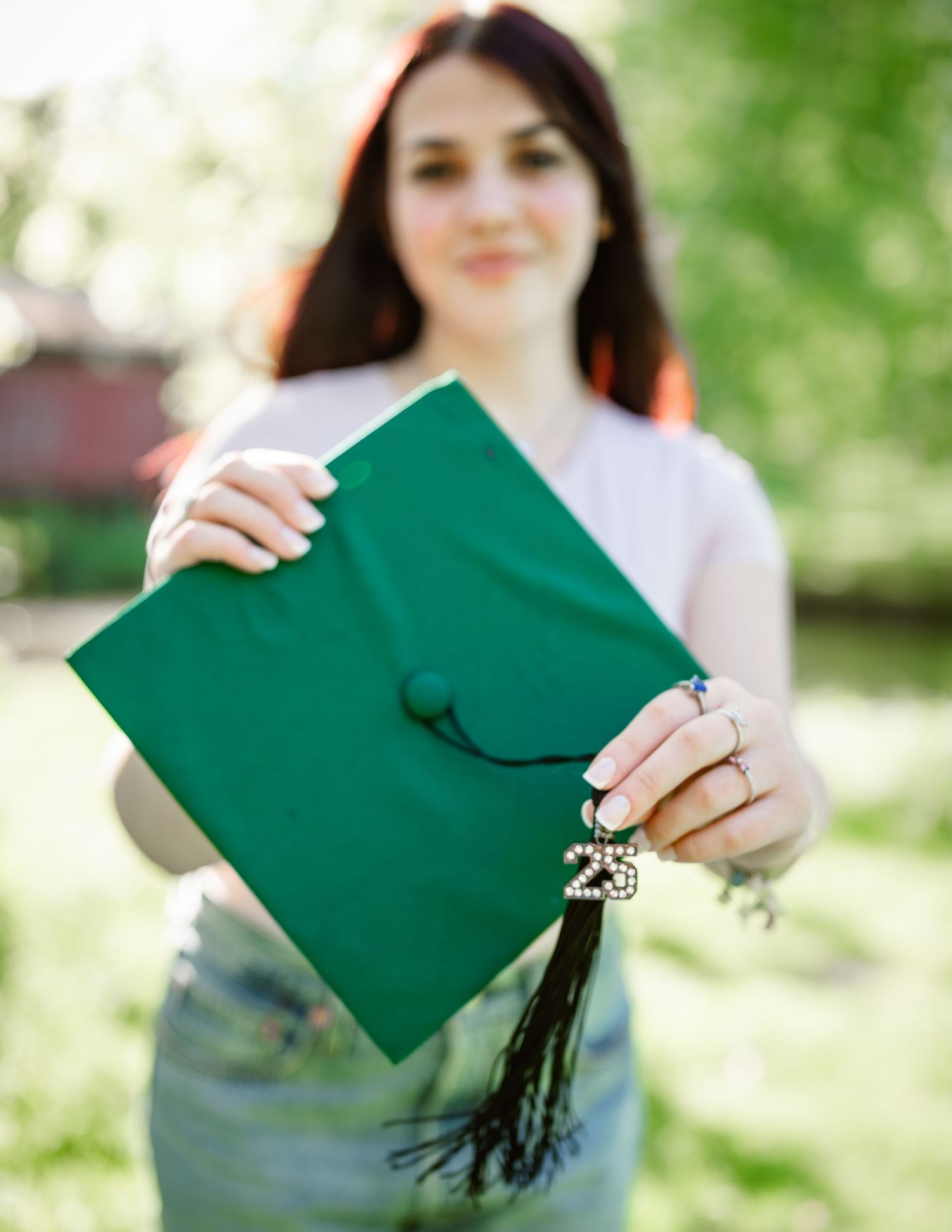 Graduate holding green diploma cover in outdoor graduation photo series.
