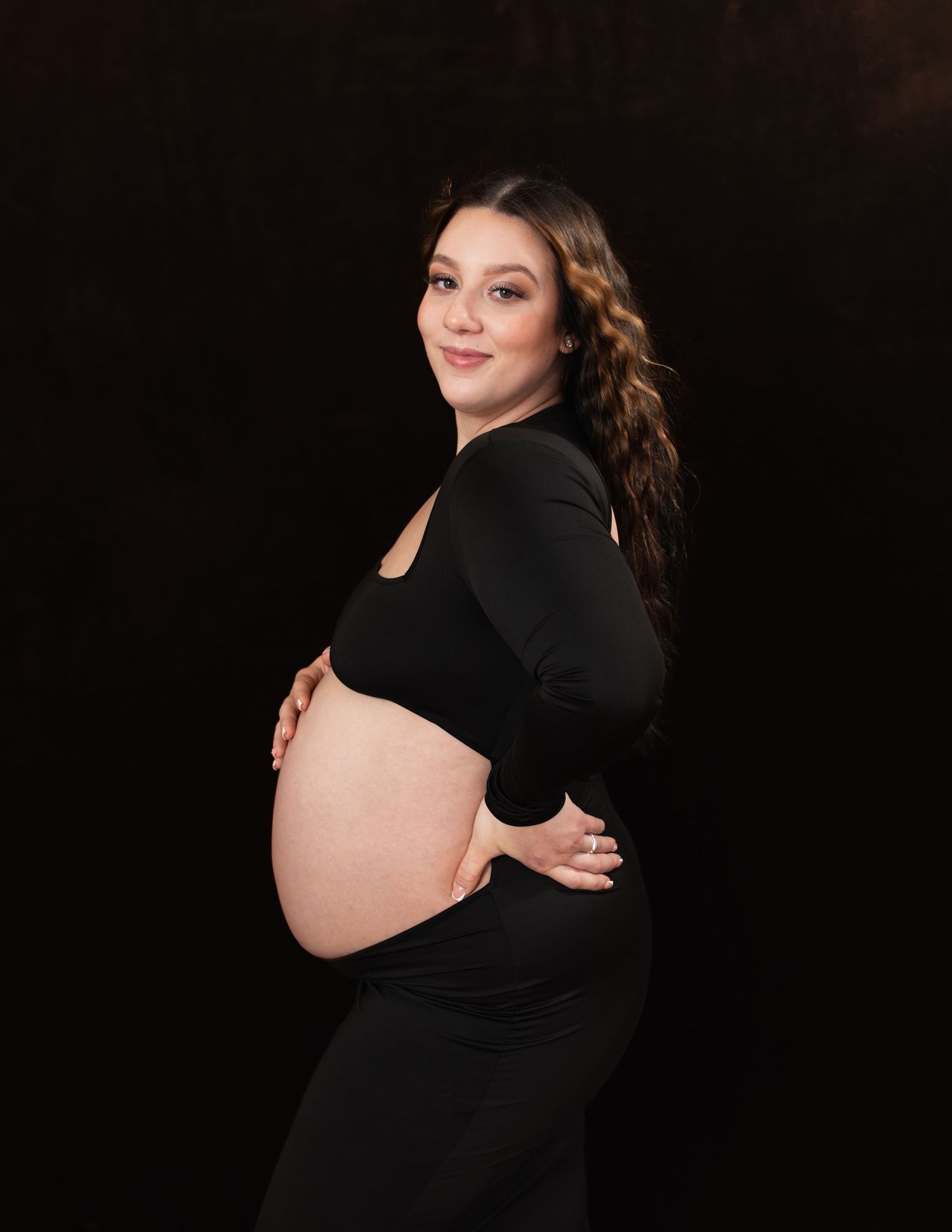 Artistic maternity portraits on black background highlighting pregnancy silhouette.