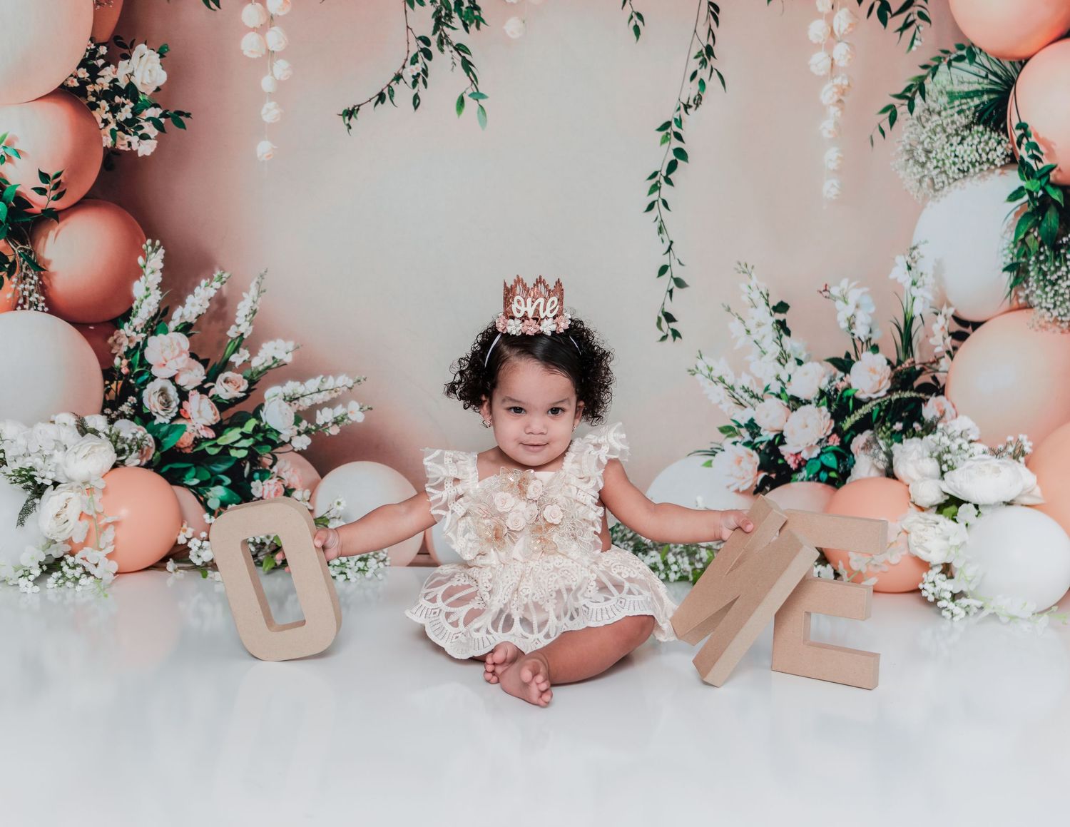 Cake smash photo session with delicate floral decorations and pink balloon garland.