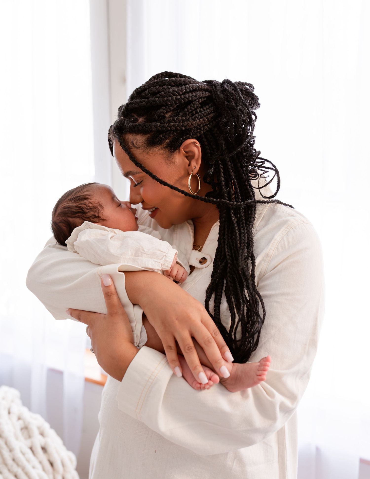 A tender moment between parent and newborn baby dressed in white against a light background.
