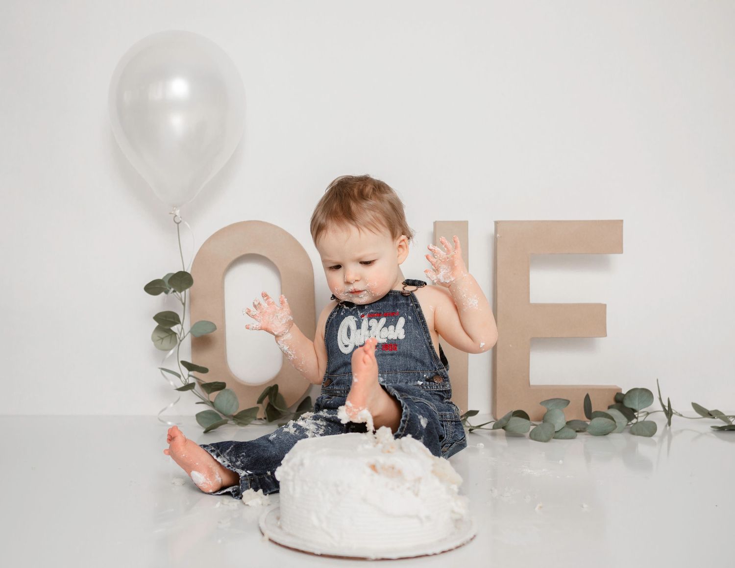 Baby in navy outfit playing with white frosted cake during first birthday photoshoot.