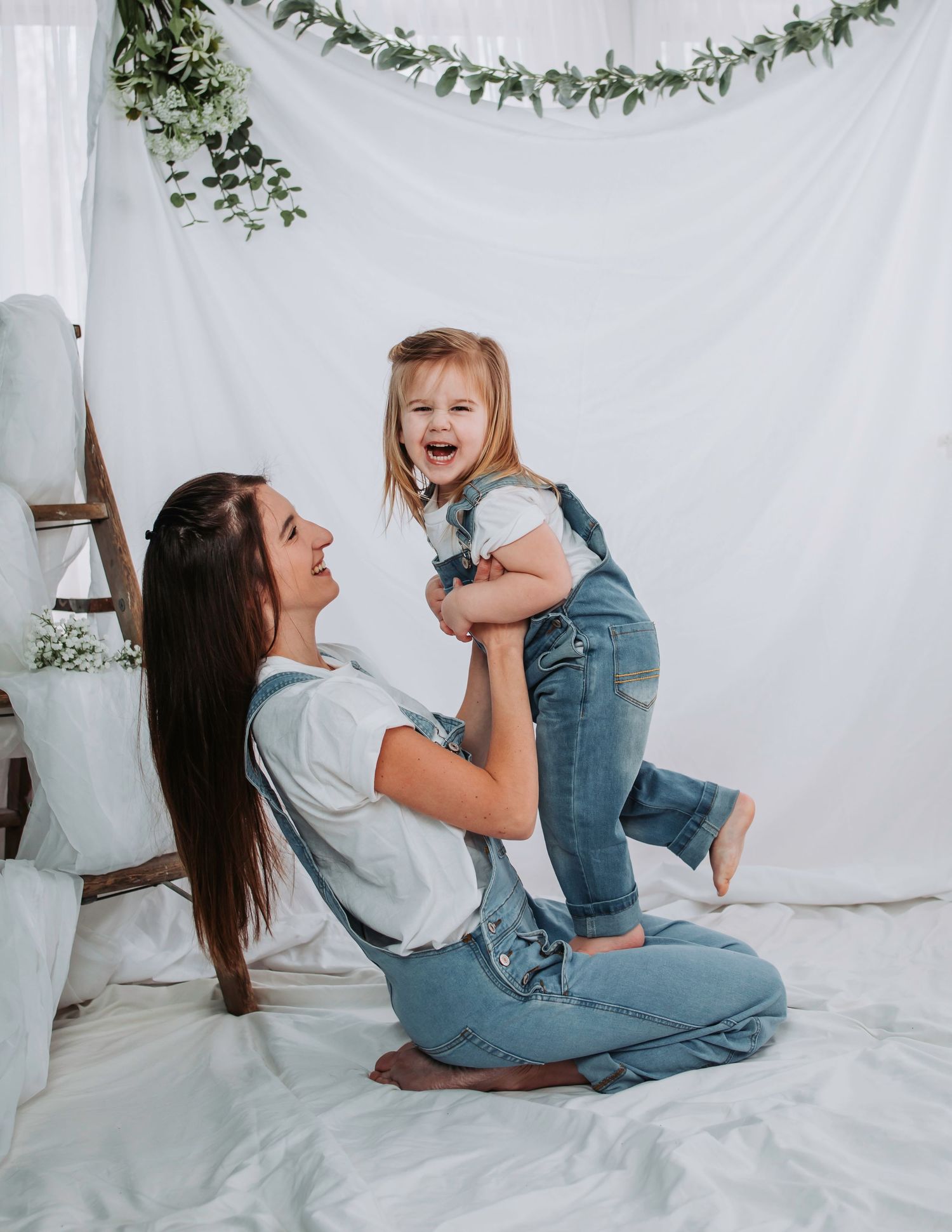 Parent and child share playful moments on white backdrop with greenery garland decoration.