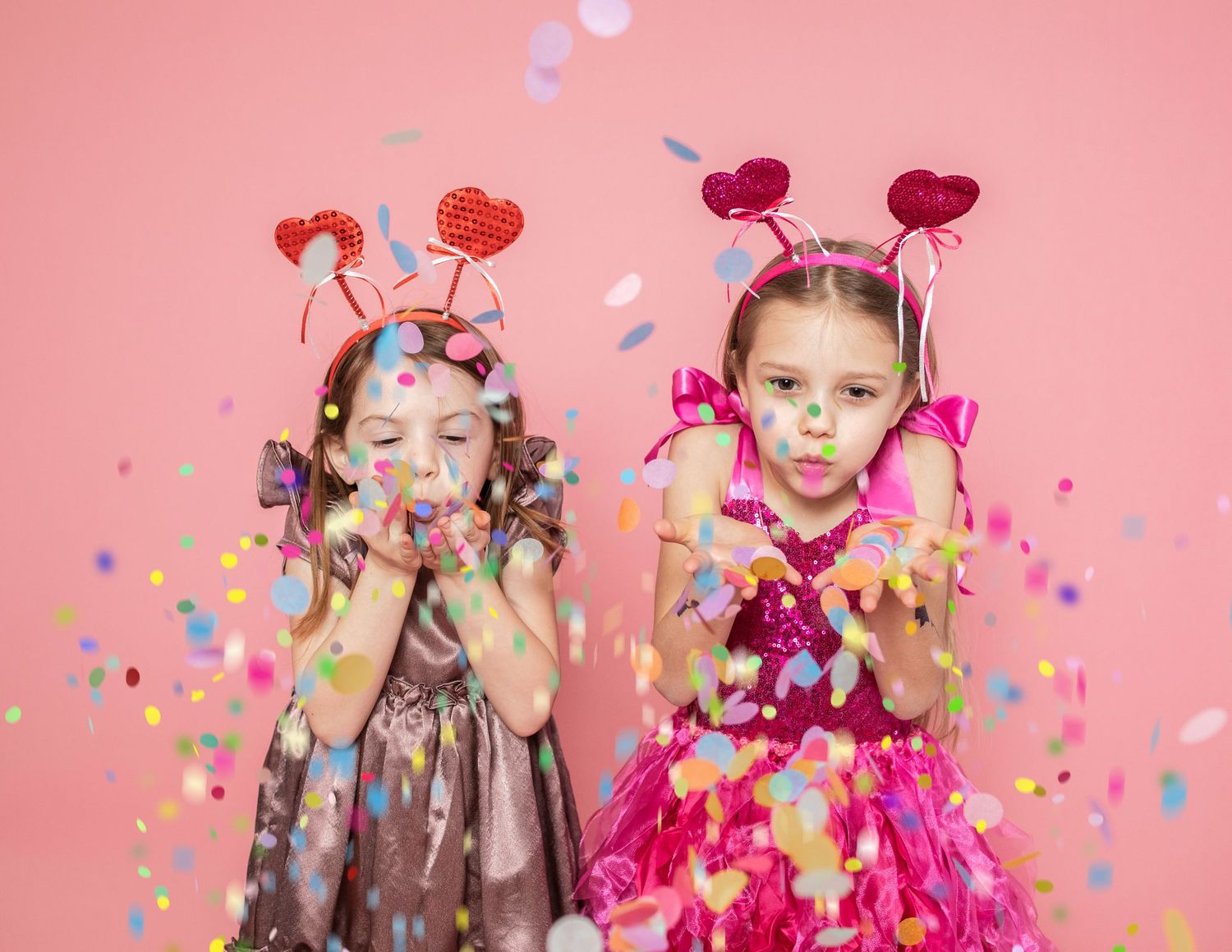 Children celebrating with confetti and party decorations against pink backdrop.