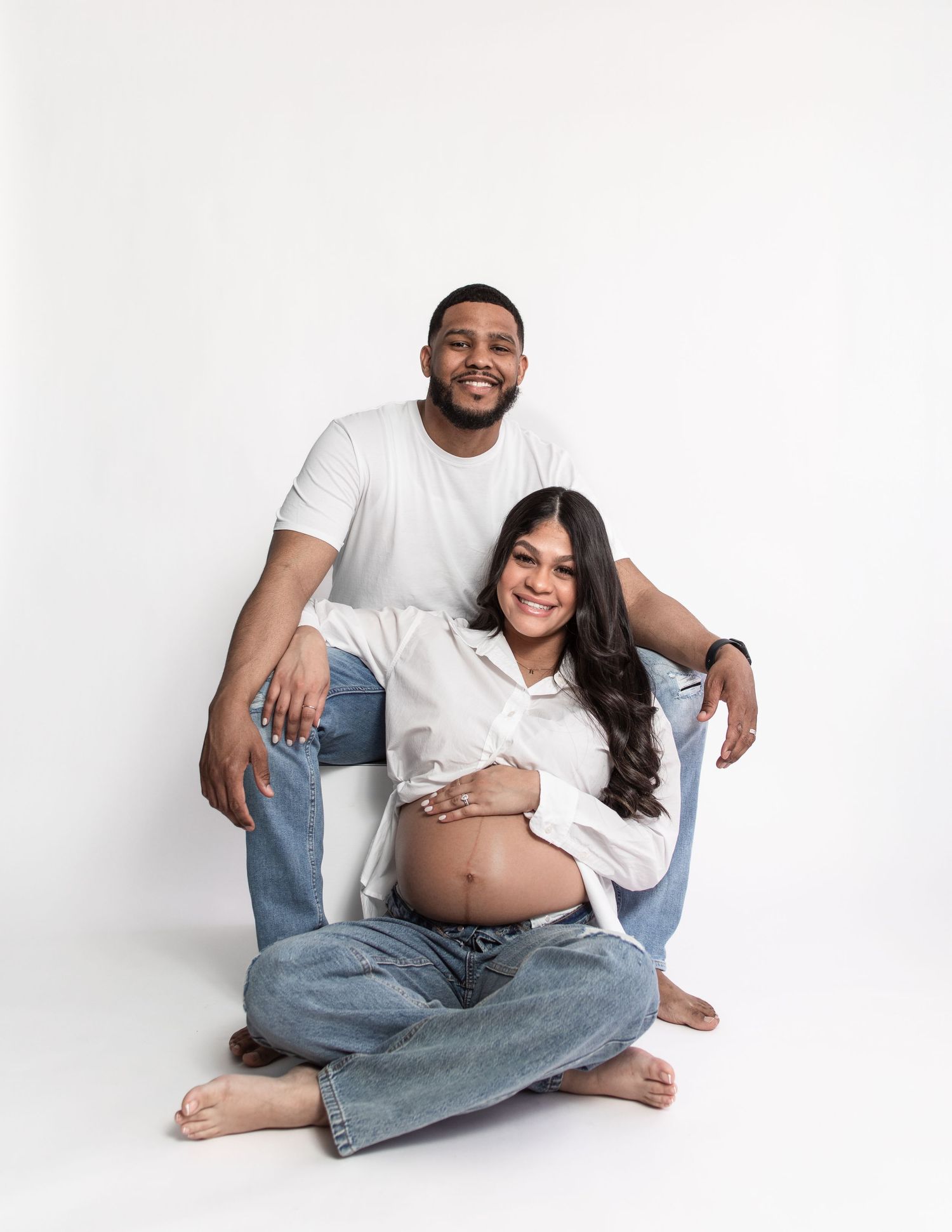 Relaxed maternity photoshoot with couple in casual attire on white background.