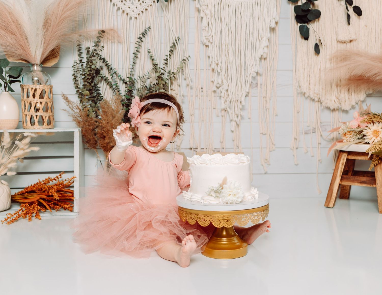 First birthday celebration setup with pink tulle dress and wooden decorations against white backdrop.