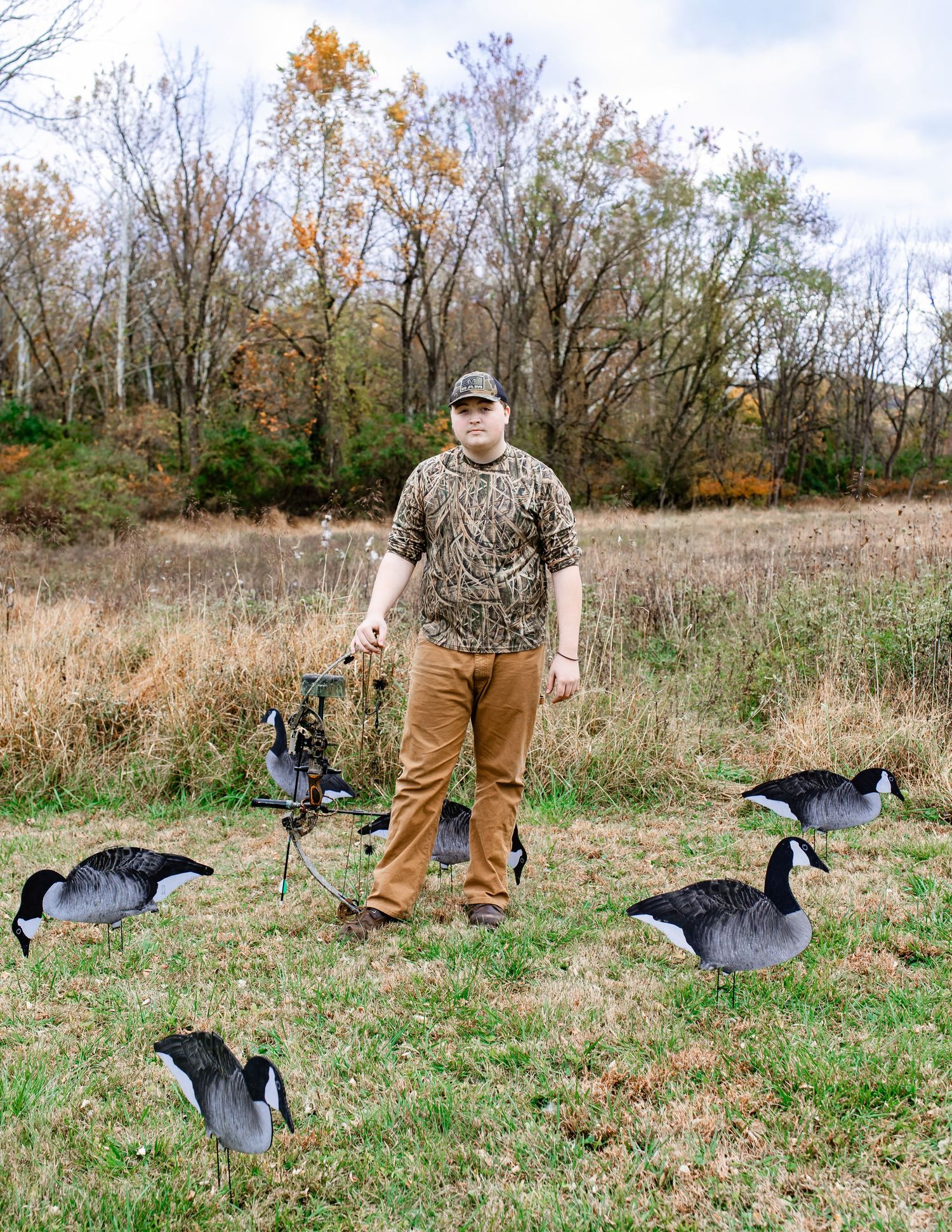 Hunter in camo gear with decoy geese set up in grassy field during hunting season.