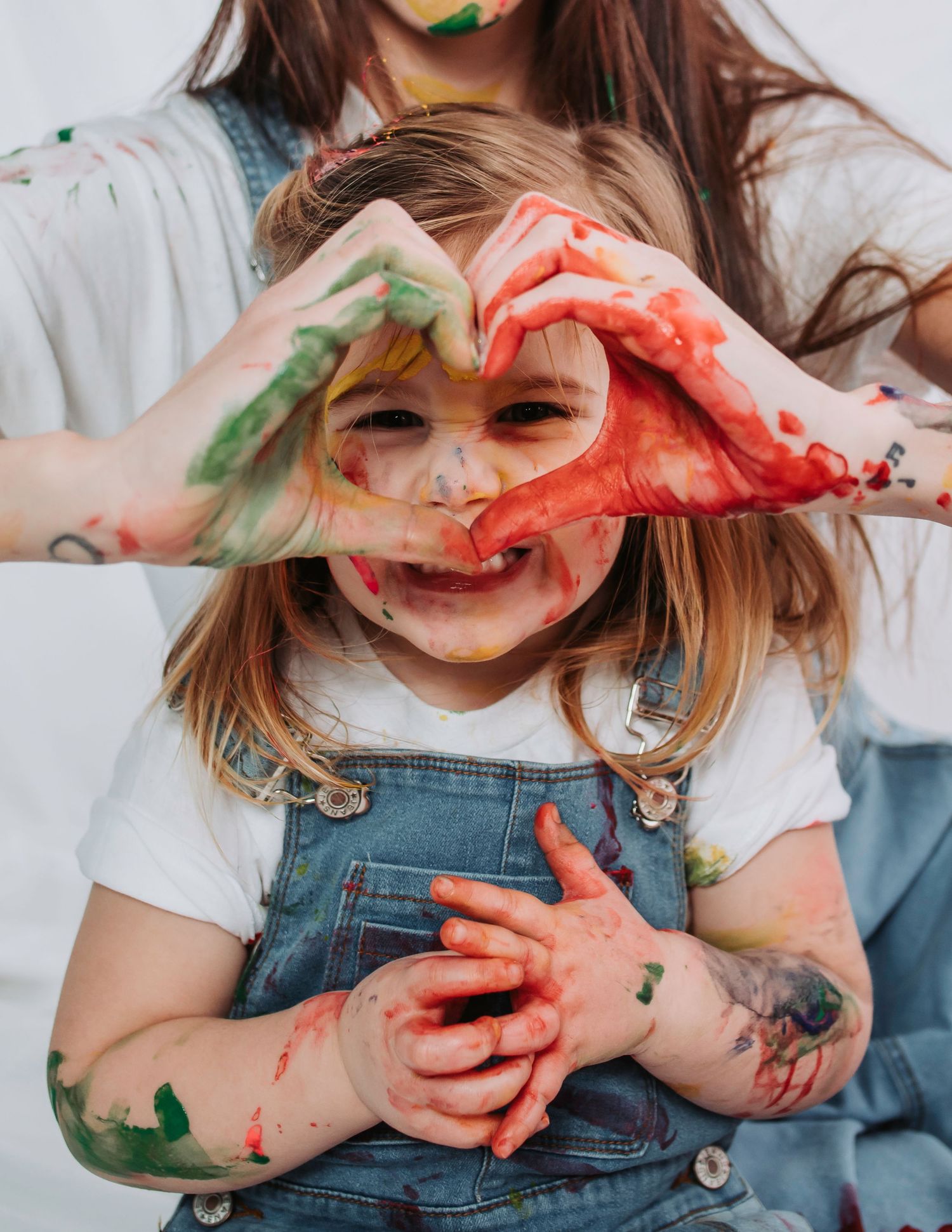 A joyful messy art session with paint-covered hands making heart shapes and wearing denim overalls.