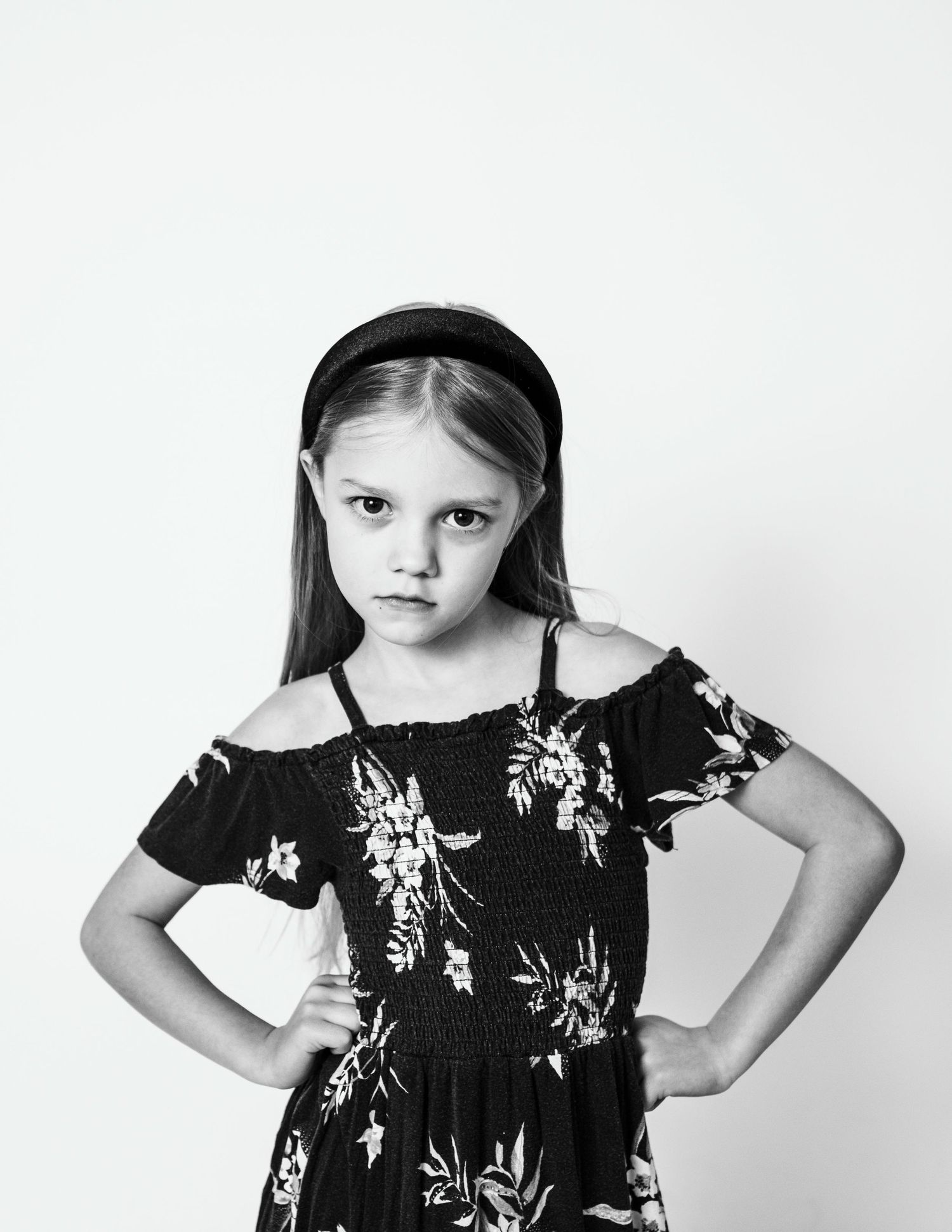 A black and white portrait with hands on hips in a floral off-shoulder dress.