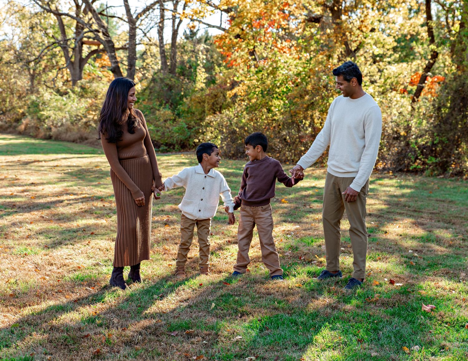 A family holds hands while walking together in an autumn park with golden foliage in the background.