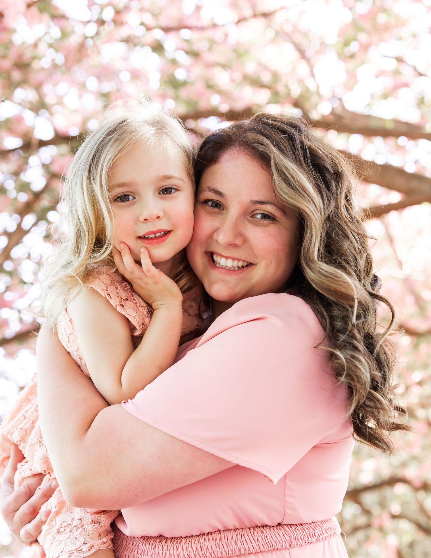 A spring portrait under cherry blossoms with soft pink tones and warm embraces.