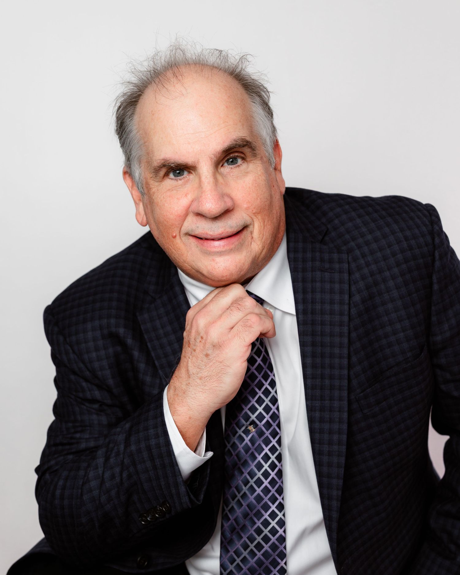 Business portrait of senior executive in dark suit with hand on chin.