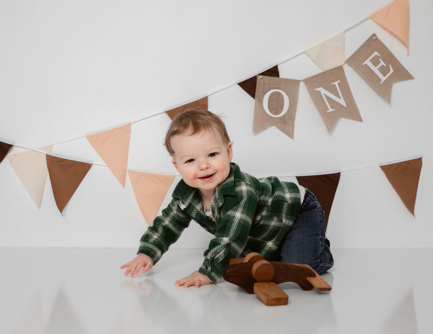 Smiling baby wearing green plaid shirt crawling under decorative bunting flags.