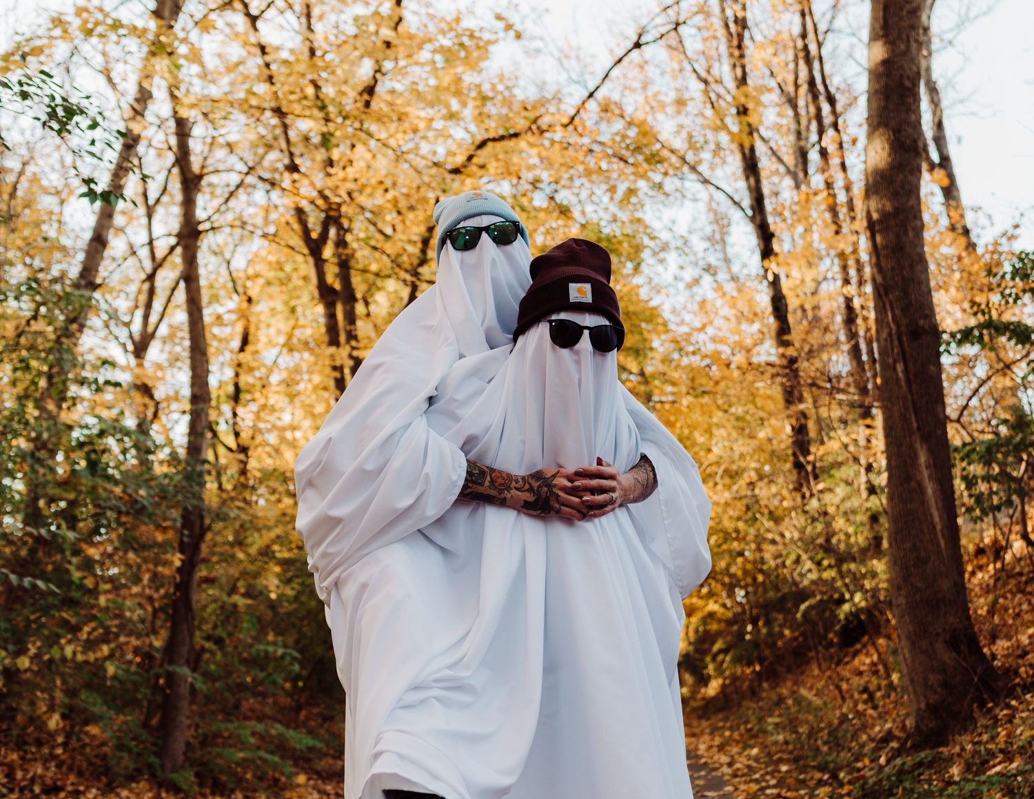 Playful ghost costumes against autumn foliage create a whimsical Halloween scene.