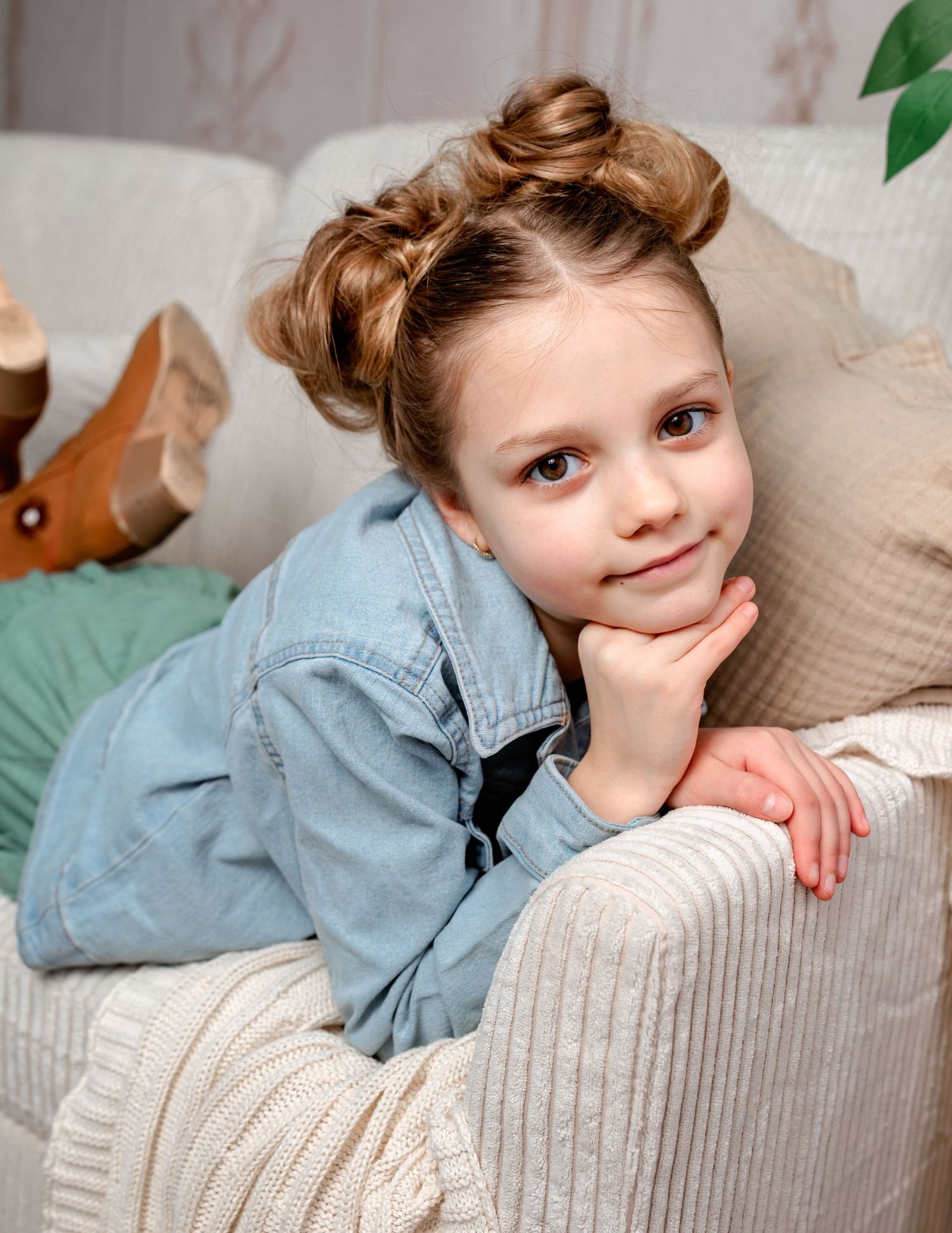 Child in denim shirt rests head on beige couch cushion in series of casual indoor portrait poses.