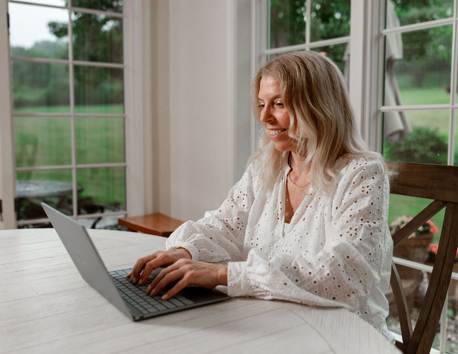 Person working on laptop in bright sunlit room with windows.